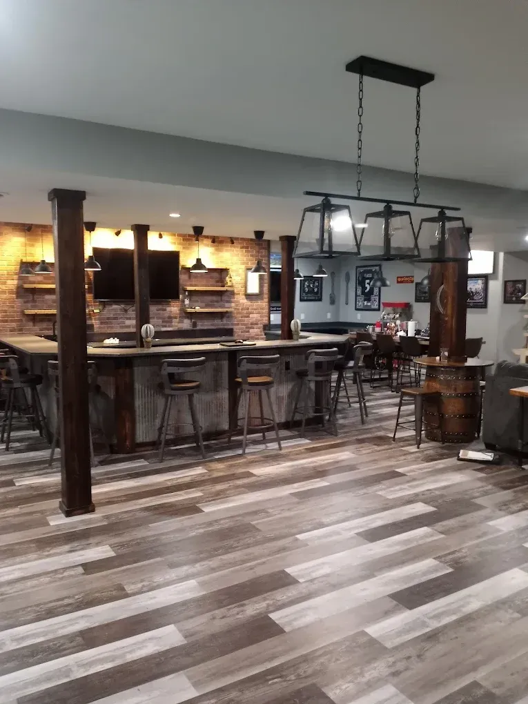 A home bar with a brick wall, wood-paneled counter, bar stools, and a hanging lantern-style light fixture.
