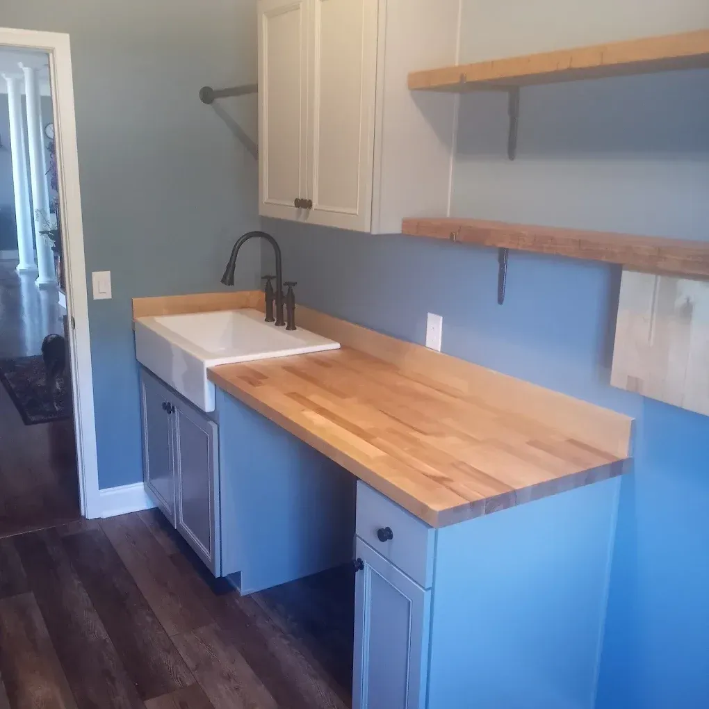 A utility room with a white farmhouse sink, butcher block counters, light blue cabinets, and wooden floating shelves.