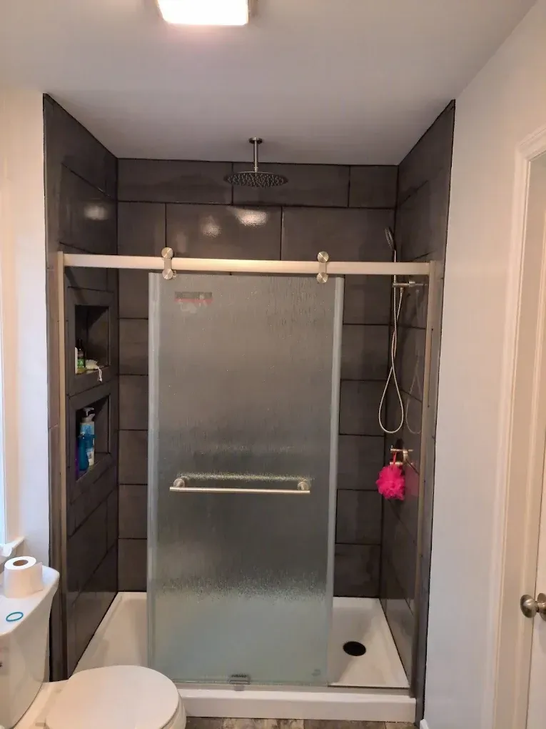 A walk-in shower with dark gray square tiles, a rainfall showerhead, frosted glass door, and two built-in wall niches.