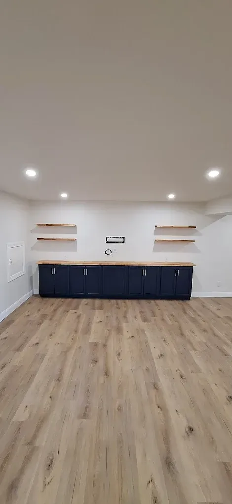 A finished room with light wood-look flooring, dark blue base cabinets, a light wood countertop, and four floating shelves.