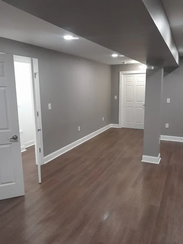 A view of a basement interior with light-colored flooring, gray walls, a support column, and two white doors.
