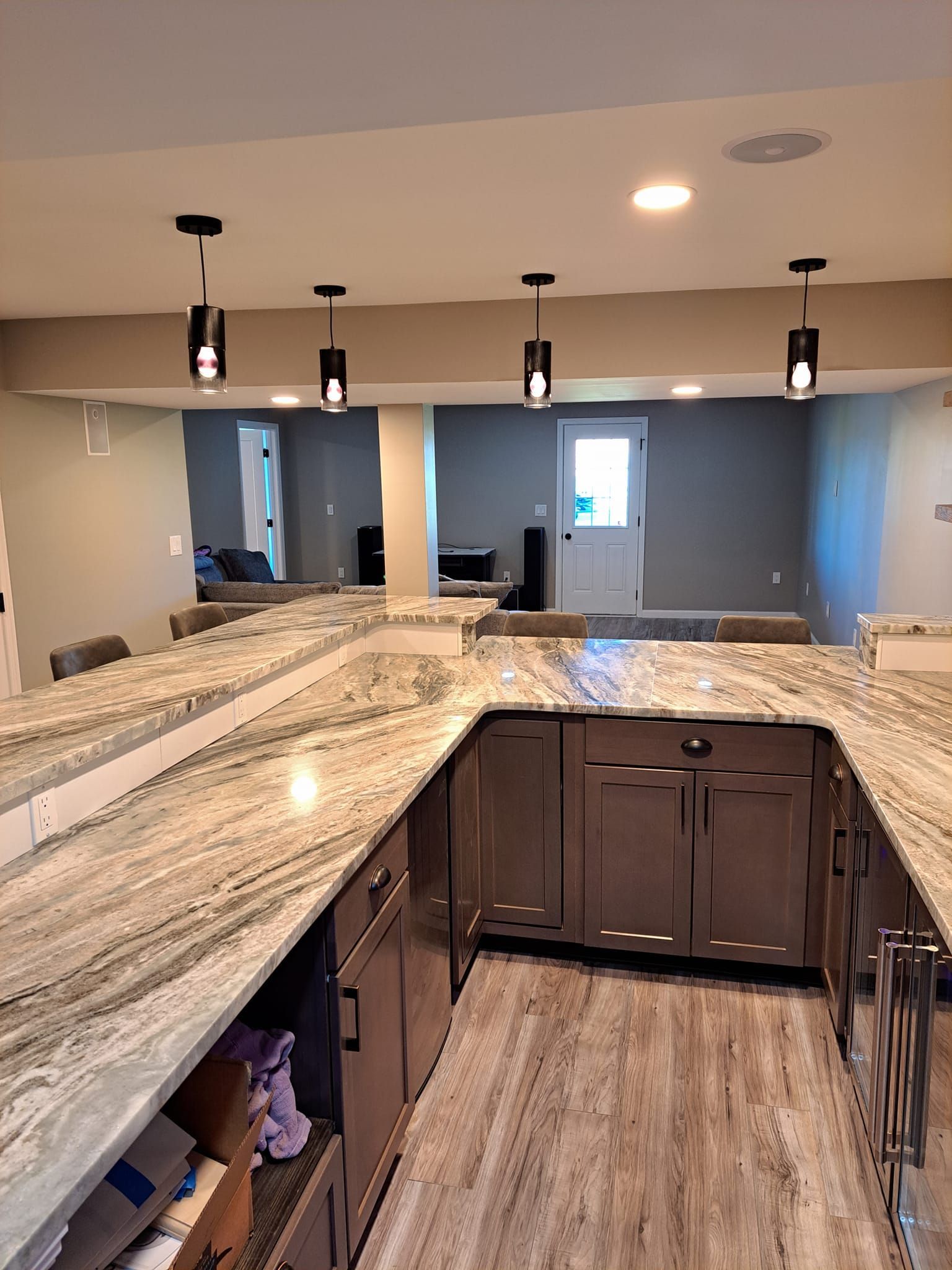 A U-shaped granite bar counter with dark wood cabinets and pendant lighting in a finished basement.