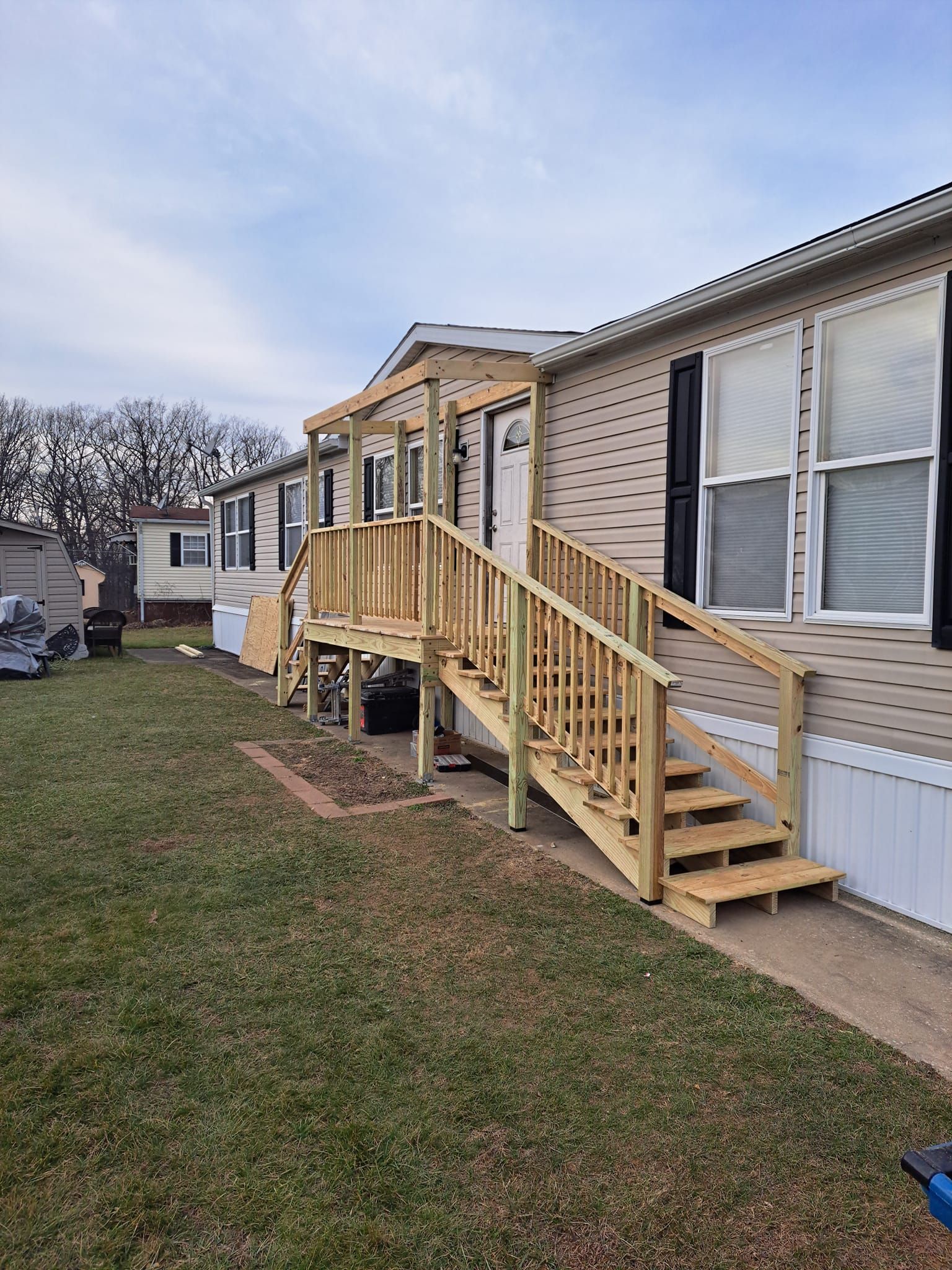 A light-colored mobile home with a newly constructed, unfinished wooden staircase and deck railing leading to the door.