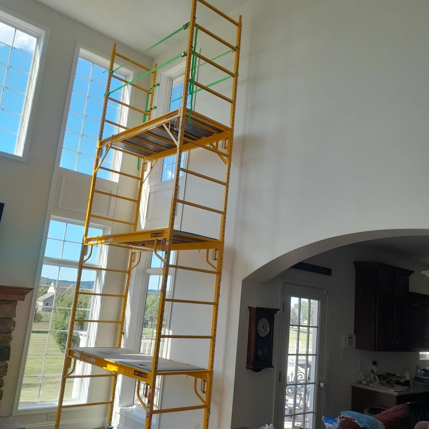 A yellow metal scaffolding tower standing in a high-ceilinged room next to large windows.
