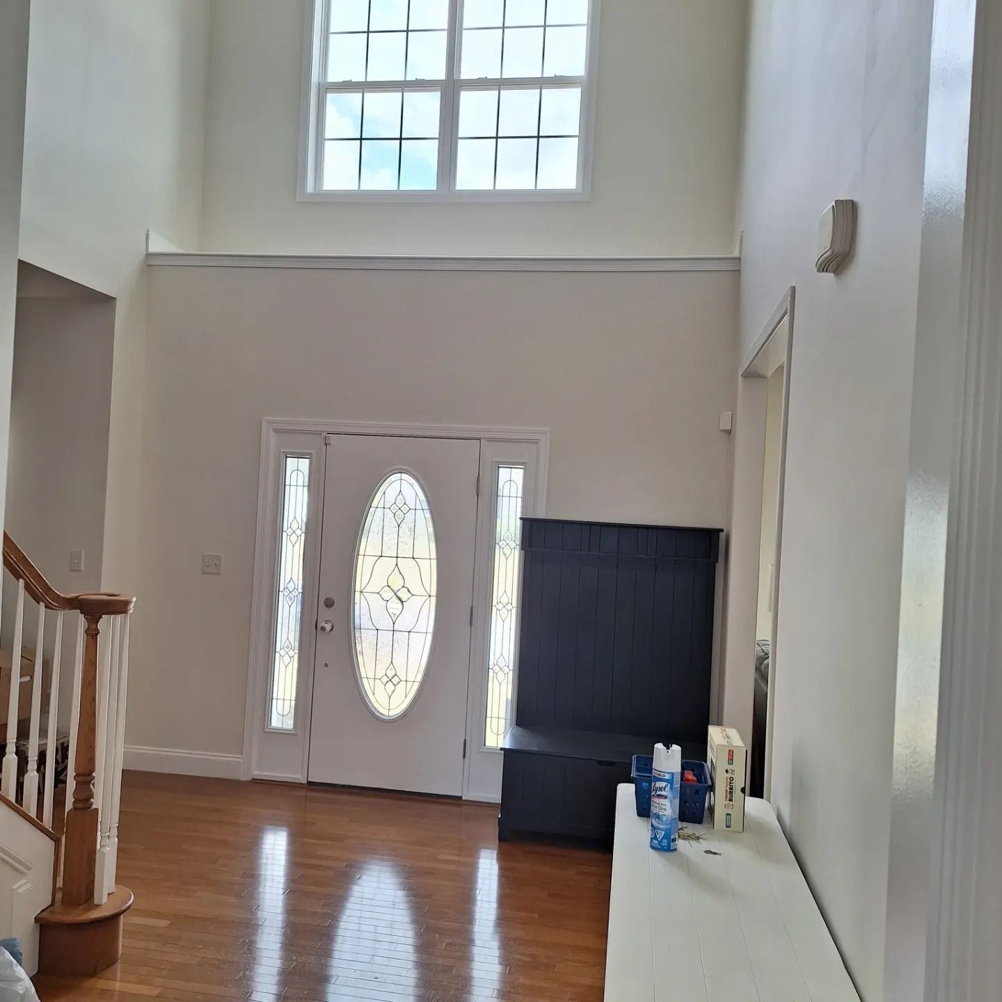 A grand entryway with hardwood floors, a white door with an oval stained-glass insert, a high window, and a dark bench.
