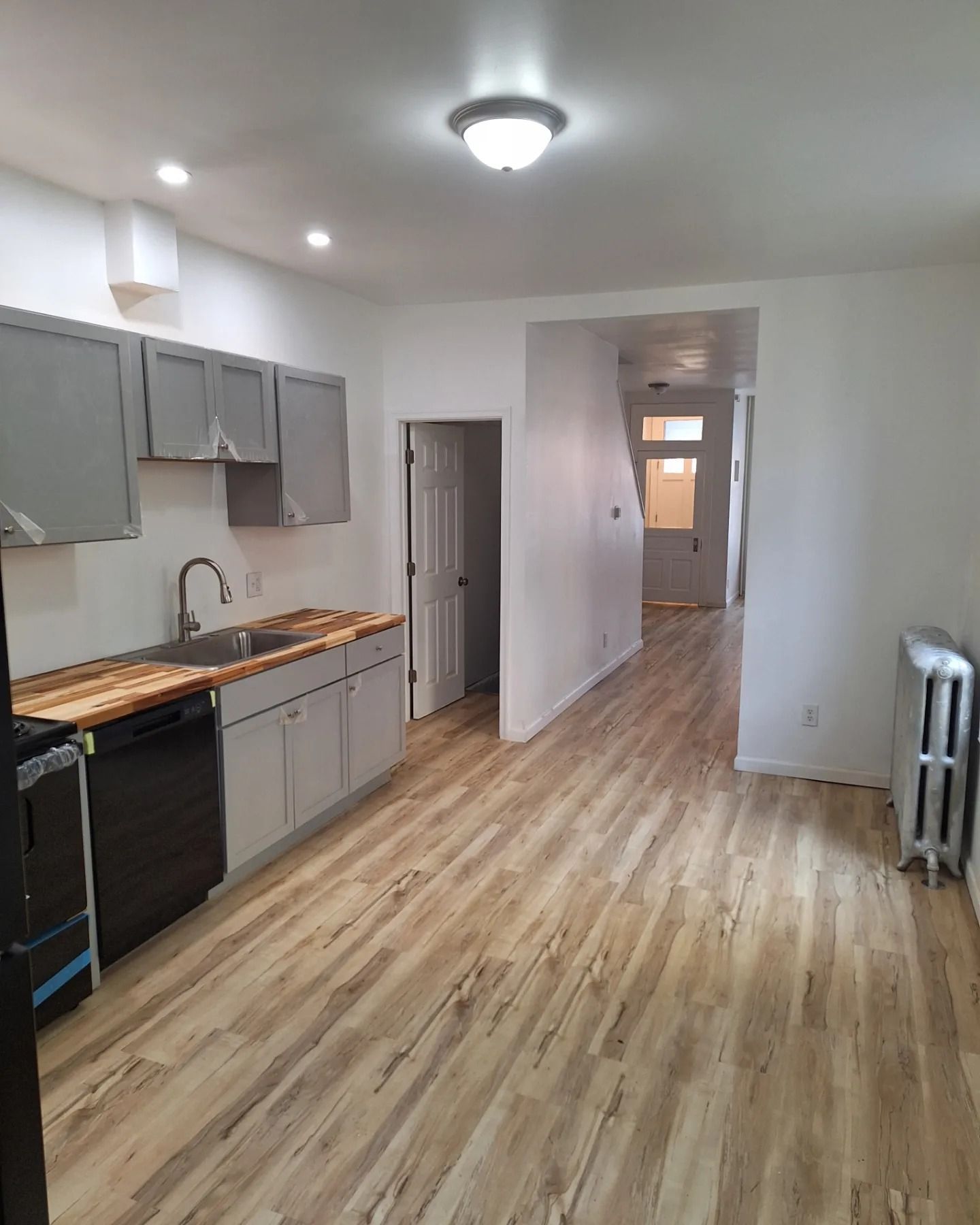 A galley-style kitchen with gray cabinets, wooden countertops, and light wood-look flooring leading to a hallway.
