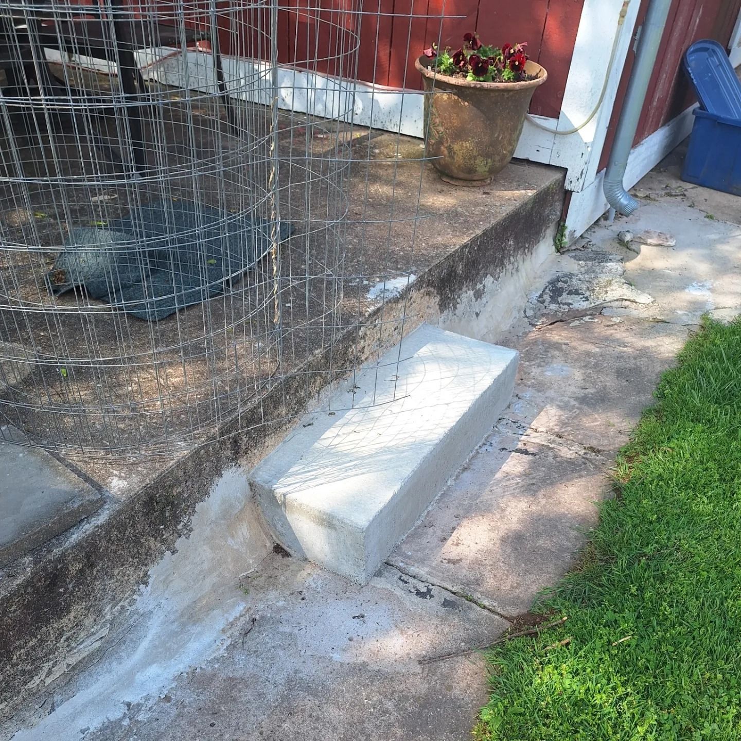 A concrete step block placed at the base of a porch next to a wire plant cage and a potted flower.