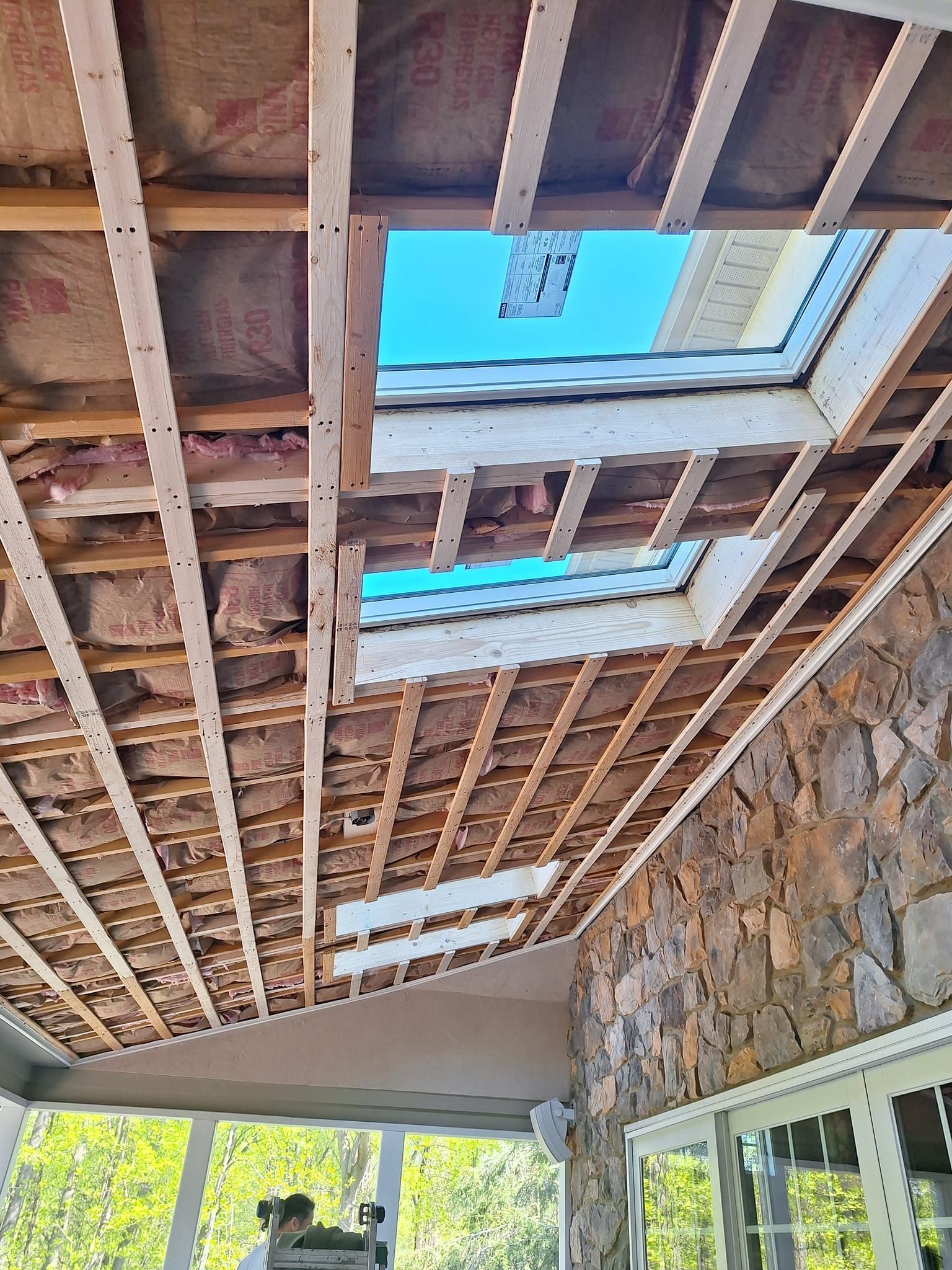 Under construction ceiling with wood framing, insulation, and multiple skylights overlooking a stone-walled room.