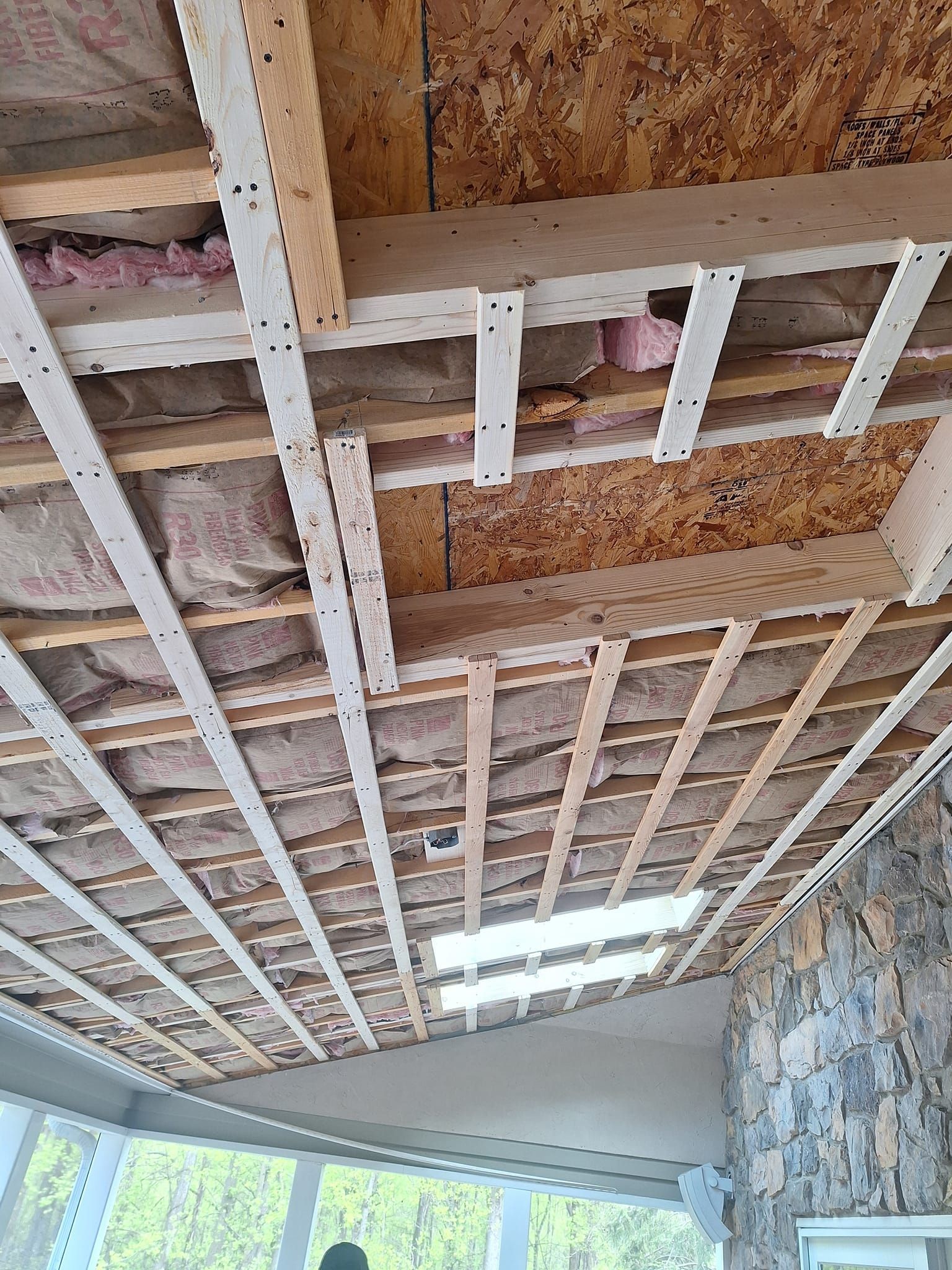 An unfinished ceiling showing wooden joists, insulation, and a skylight above a stone wall interior.