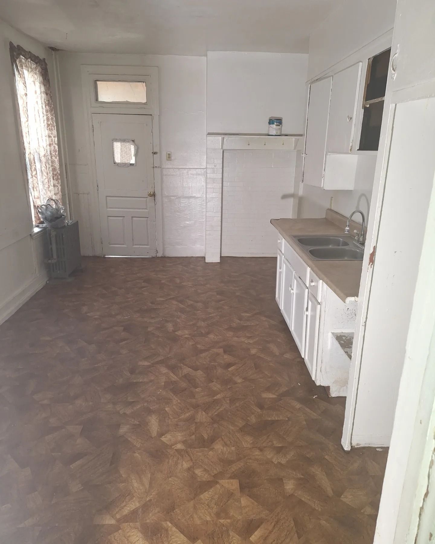 Empty kitchen featuring white cabinets, a sink, a door with a window, and brown patterned flooring.