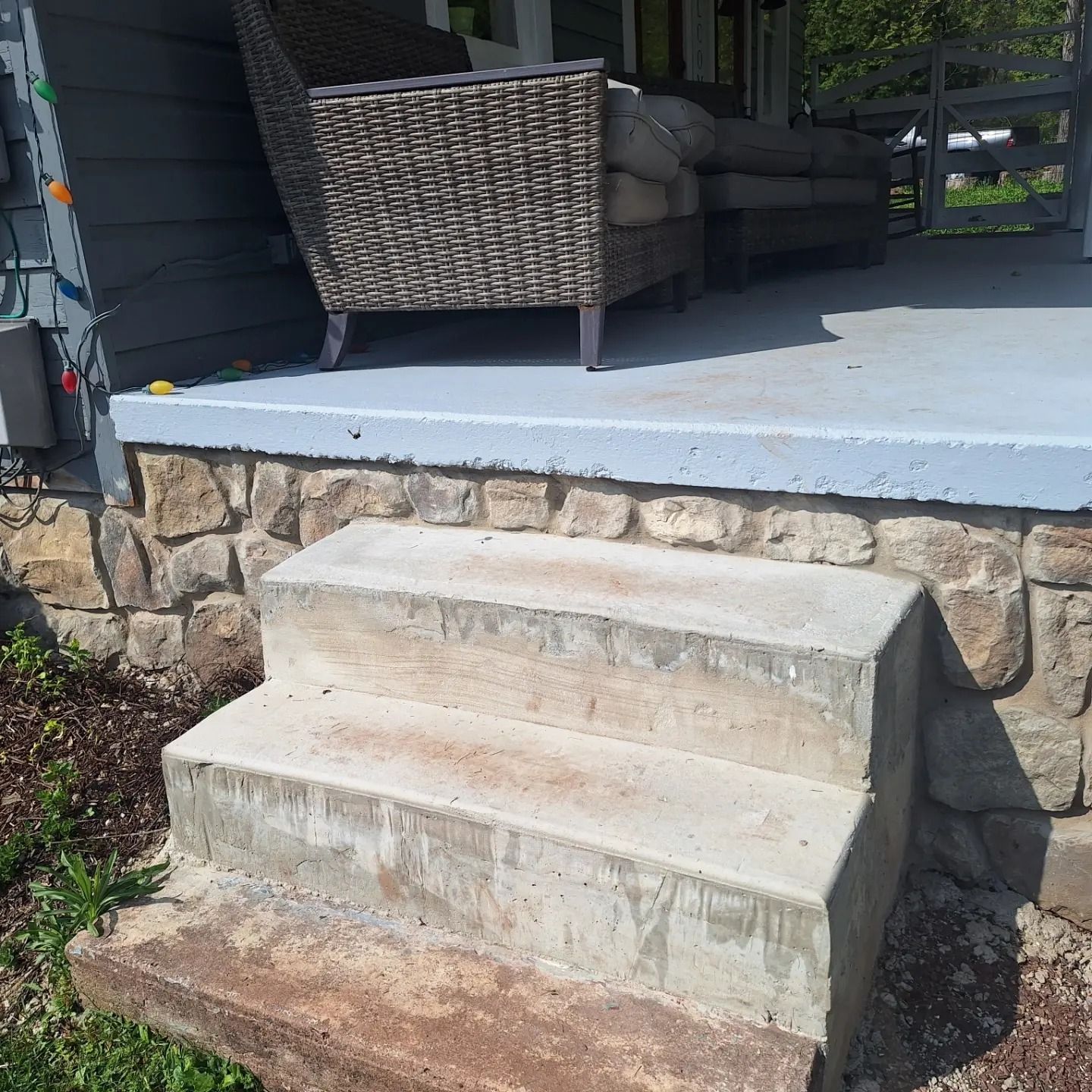 Two concrete steps leading up to a stone-walled porch with wicker patio furniture.