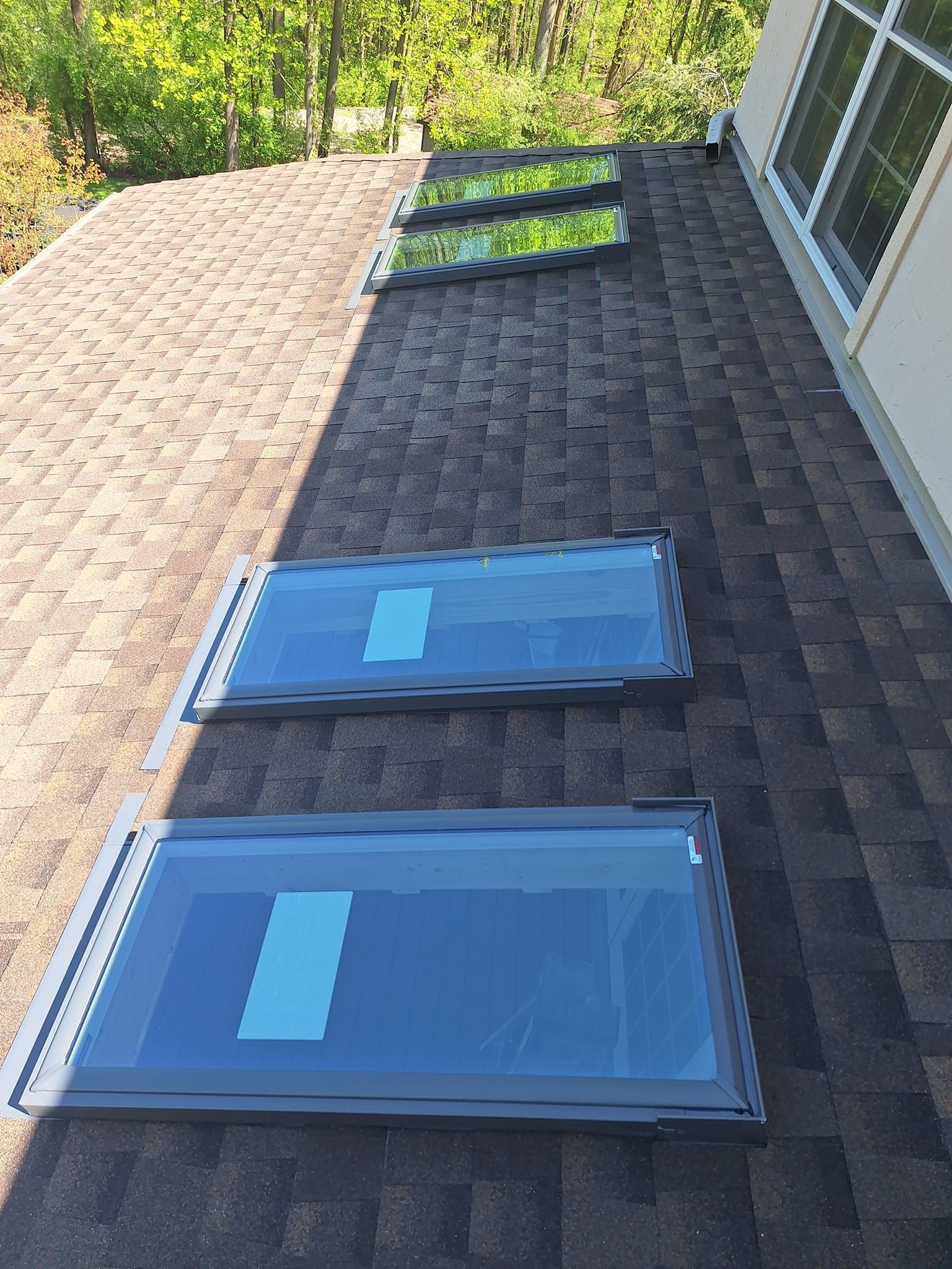 Three skylights installed on a brown shingled roof next to the exterior wall of a house.