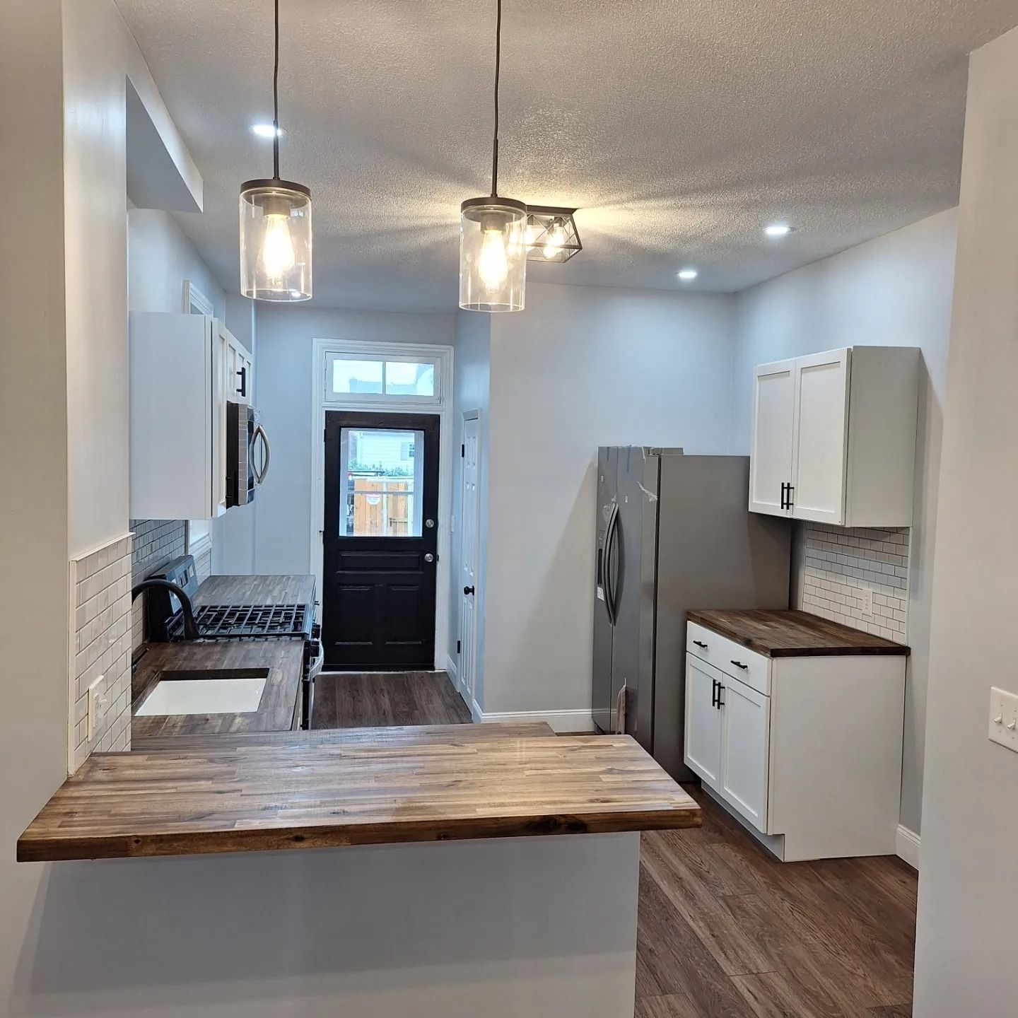 A modern kitchen with white cabinets, dark wood countertops, stainless steel appliances, and two hanging glass pendants.