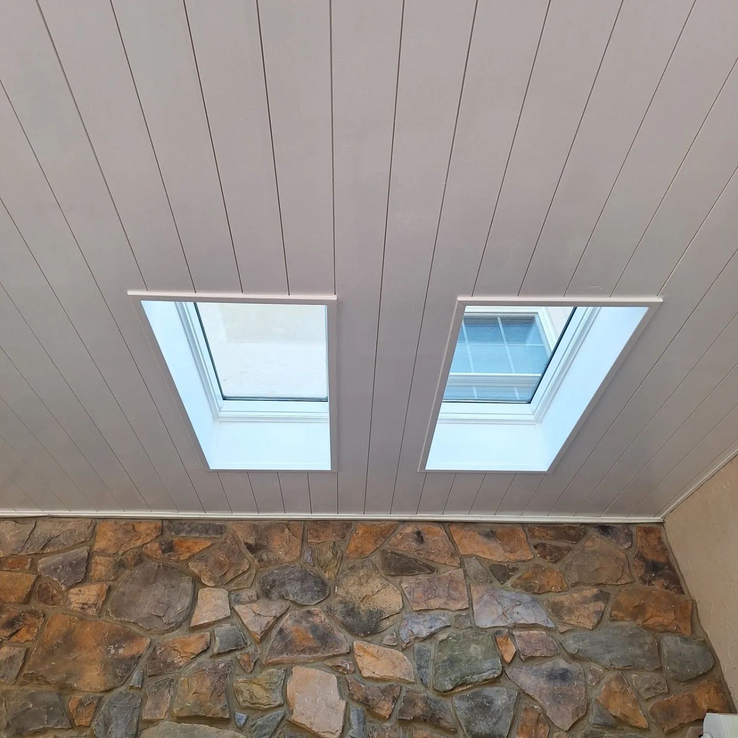Two skylights embedded in a white paneled ceiling above a wall with a textured stone finish.