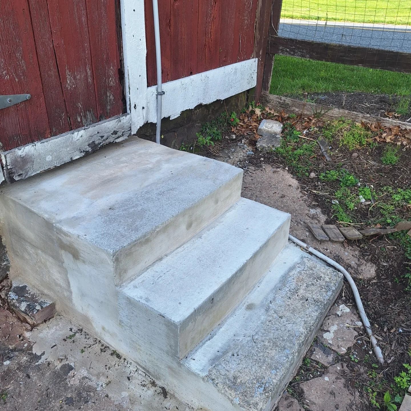 Three concrete steps lead up to a red wooden door, with a metal conduit running along the wall.