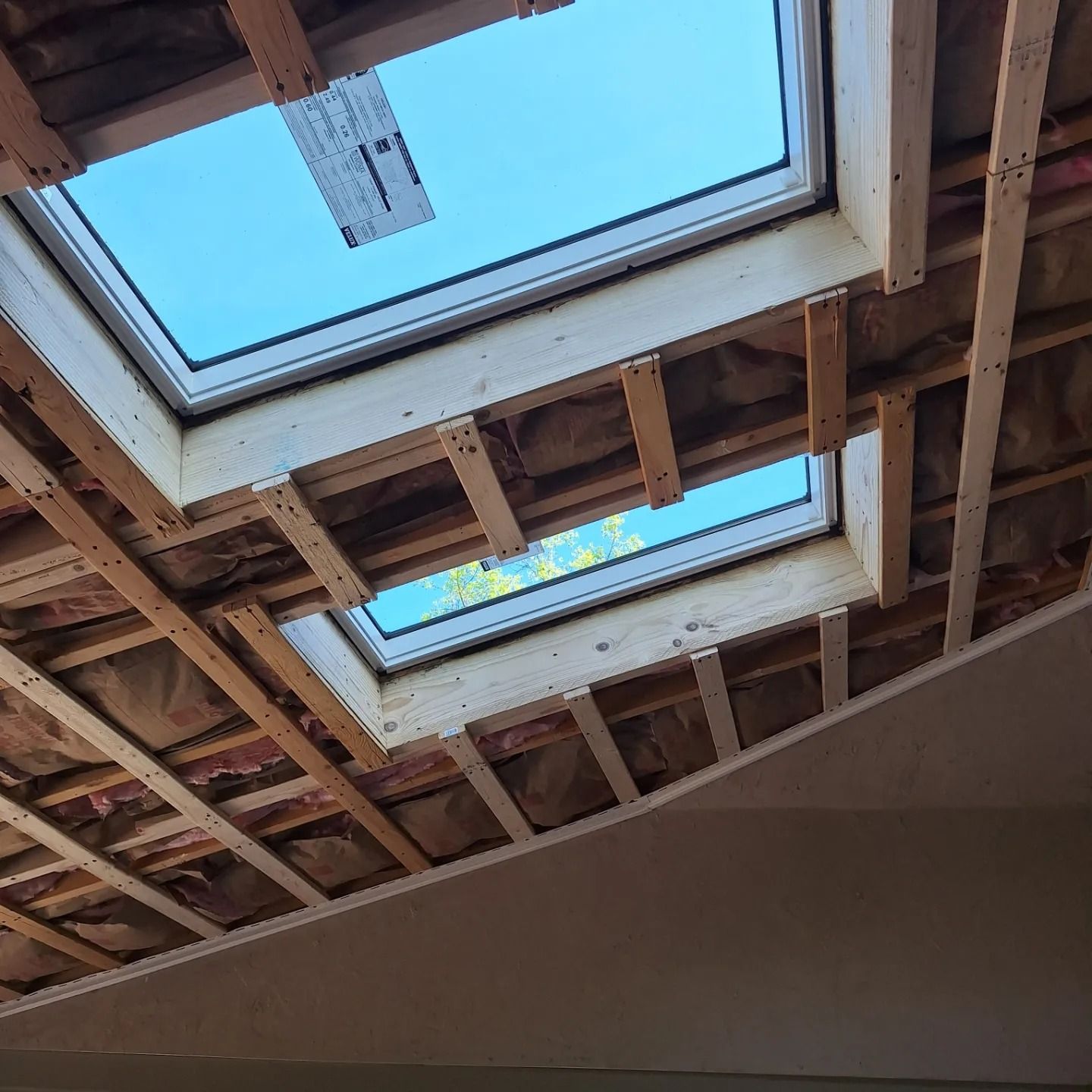 Two skylights framed by exposed wooden rafters and insulation in an unfinished ceiling during construction.