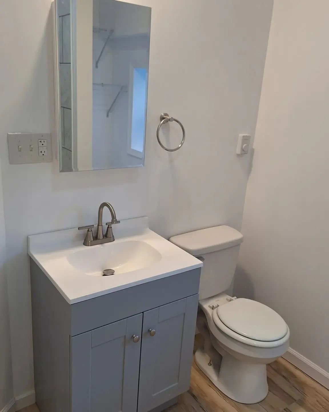 A grey bathroom vanity with a white sink and mirror cabinet next to a white toilet in a bright, minimalist bathroom.