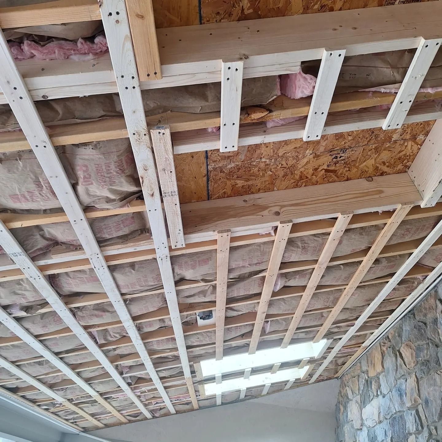 A low-angle view of a partially finished wood-framed ceiling with exposed insulation and light panels.