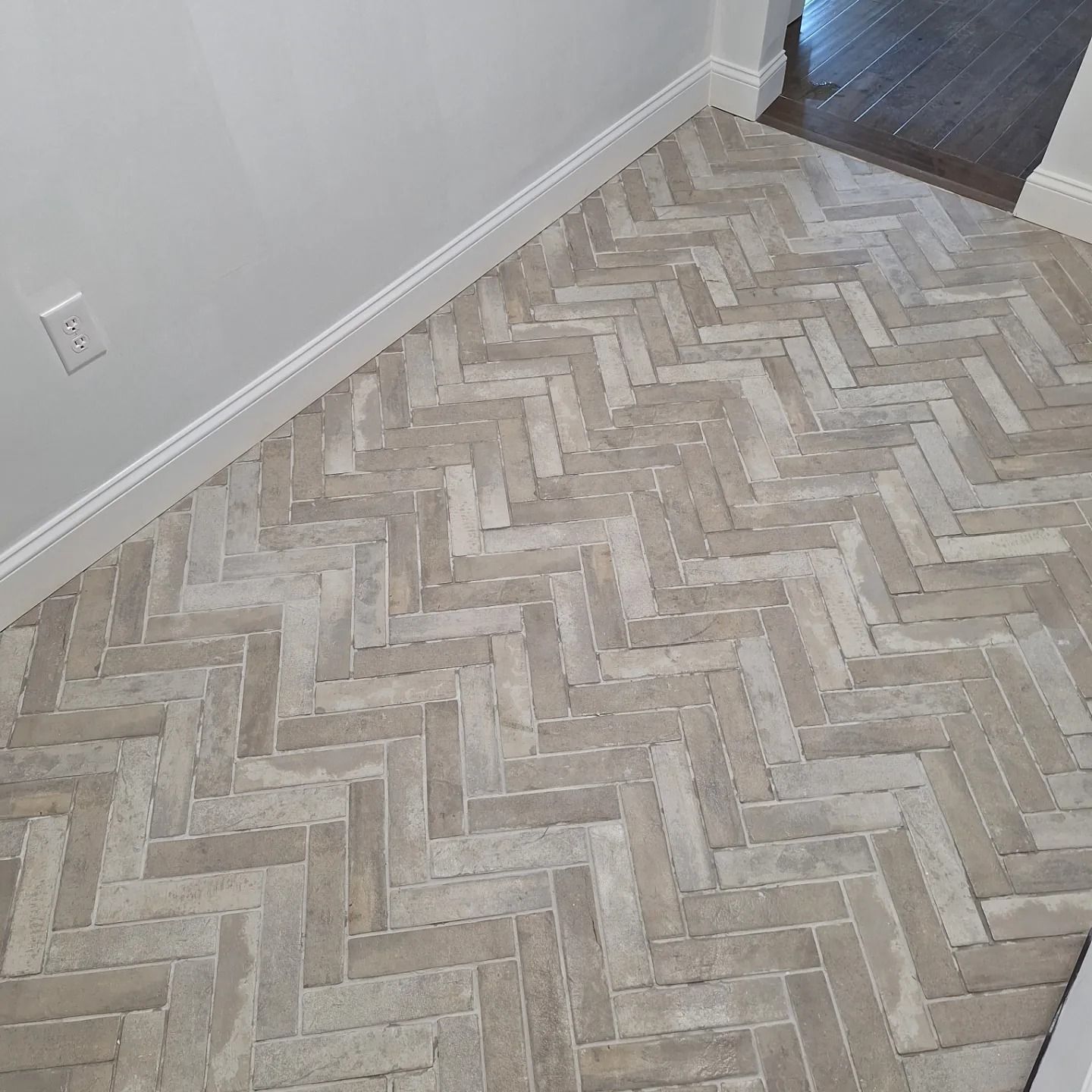 A light-colored brick floor laid in a herringbone pattern inside a home with white baseboards.