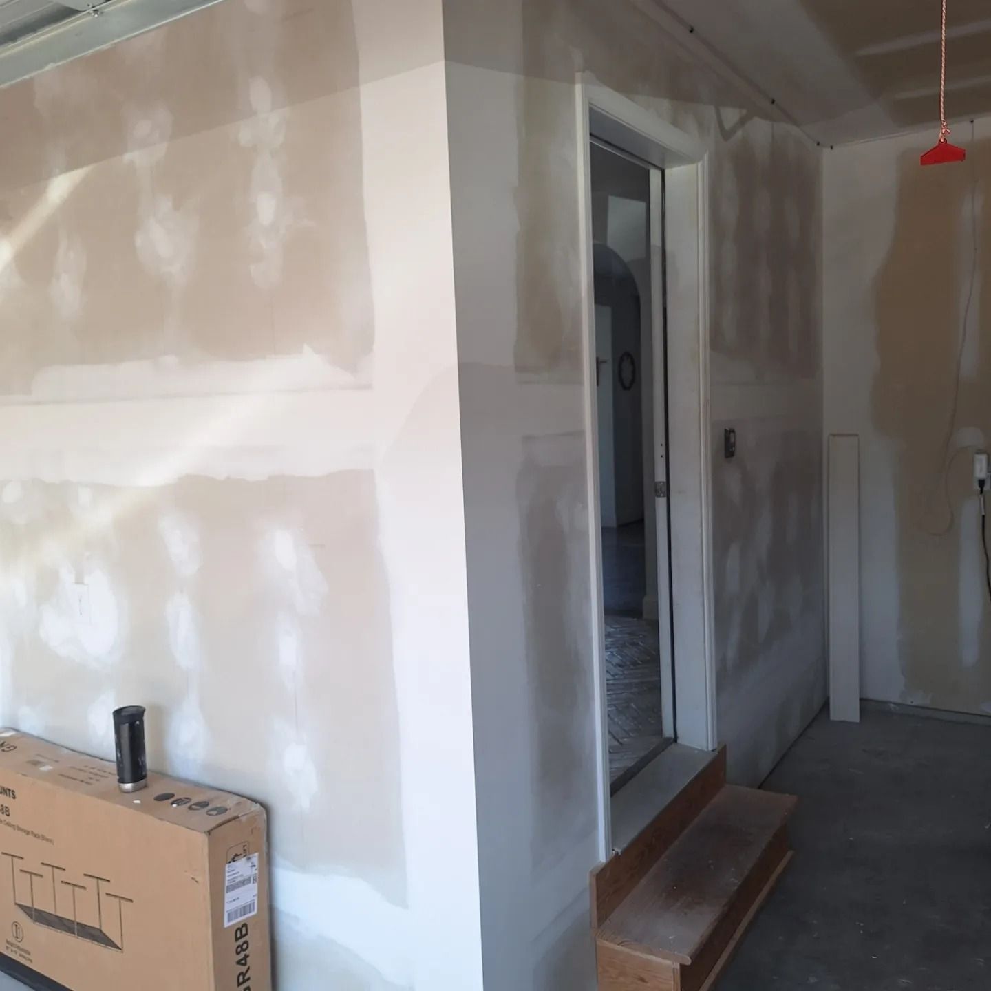 A garage interior with unfinished drywall, tape, and compound, featuring a doorway leading into a house and a cardboard box.