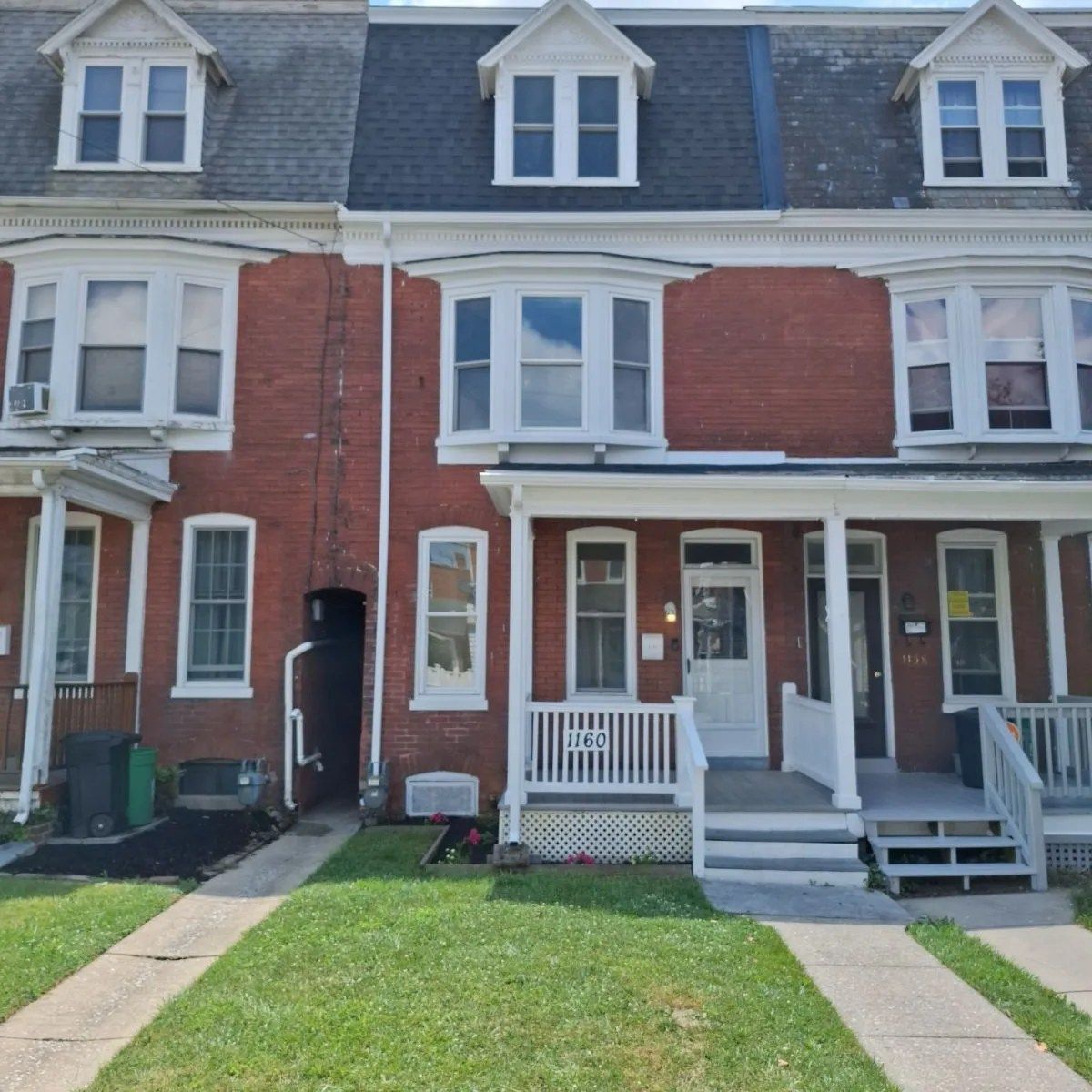 A row of red brick townhouses with multiple stories, dormer windows, bay windows, and front porches on a sunny day.