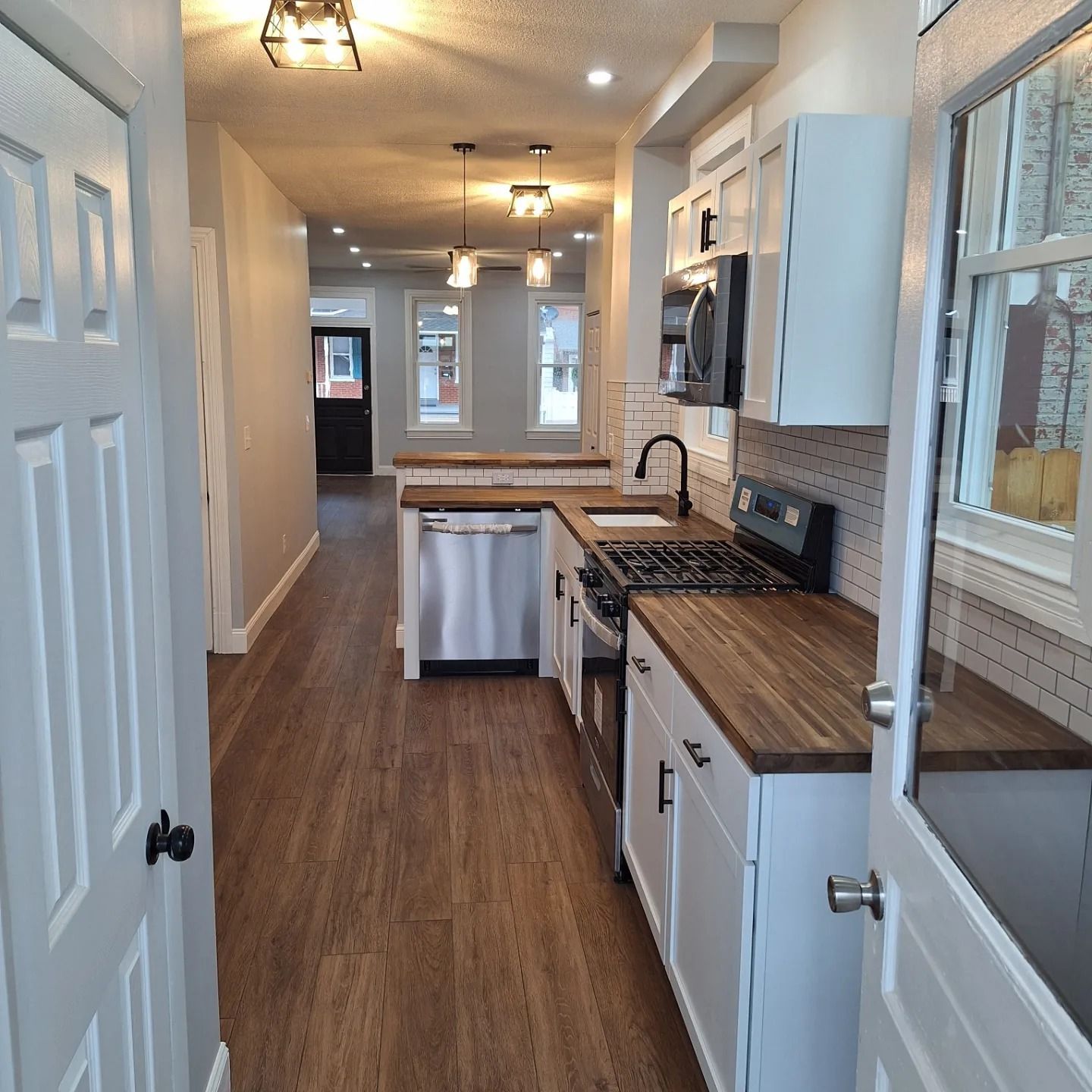 A kitchen with white cabinets, wood countertops, and stainless steel appliances, opening into a bright hallway.
