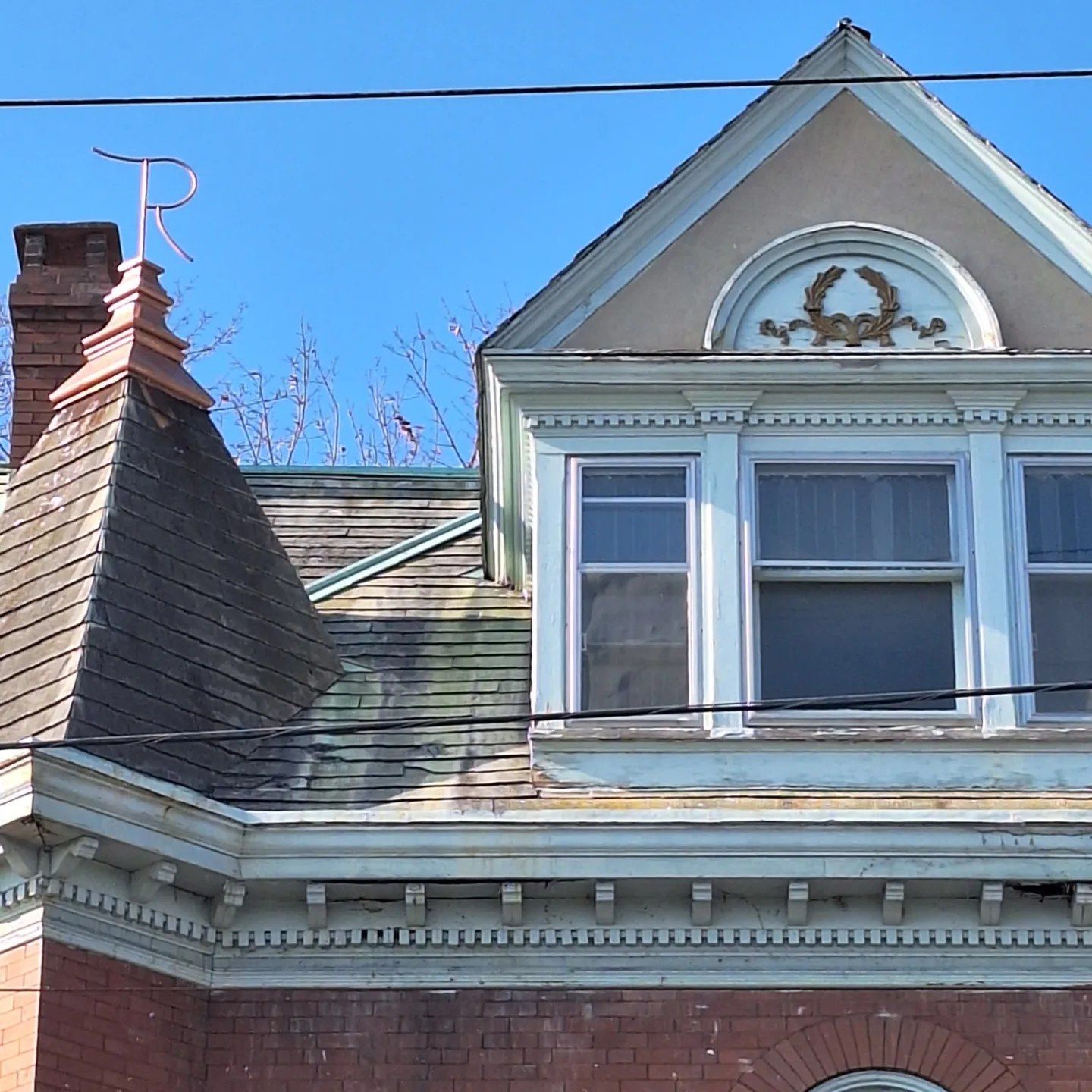 A brick Victorian house features a pointed roof tower with a copper 