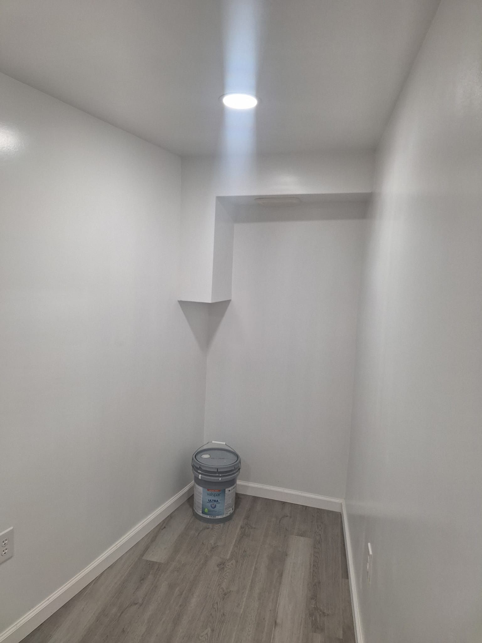 A small, empty closet with white walls, gray wood-look flooring, and a single recessed light fixture overhead.