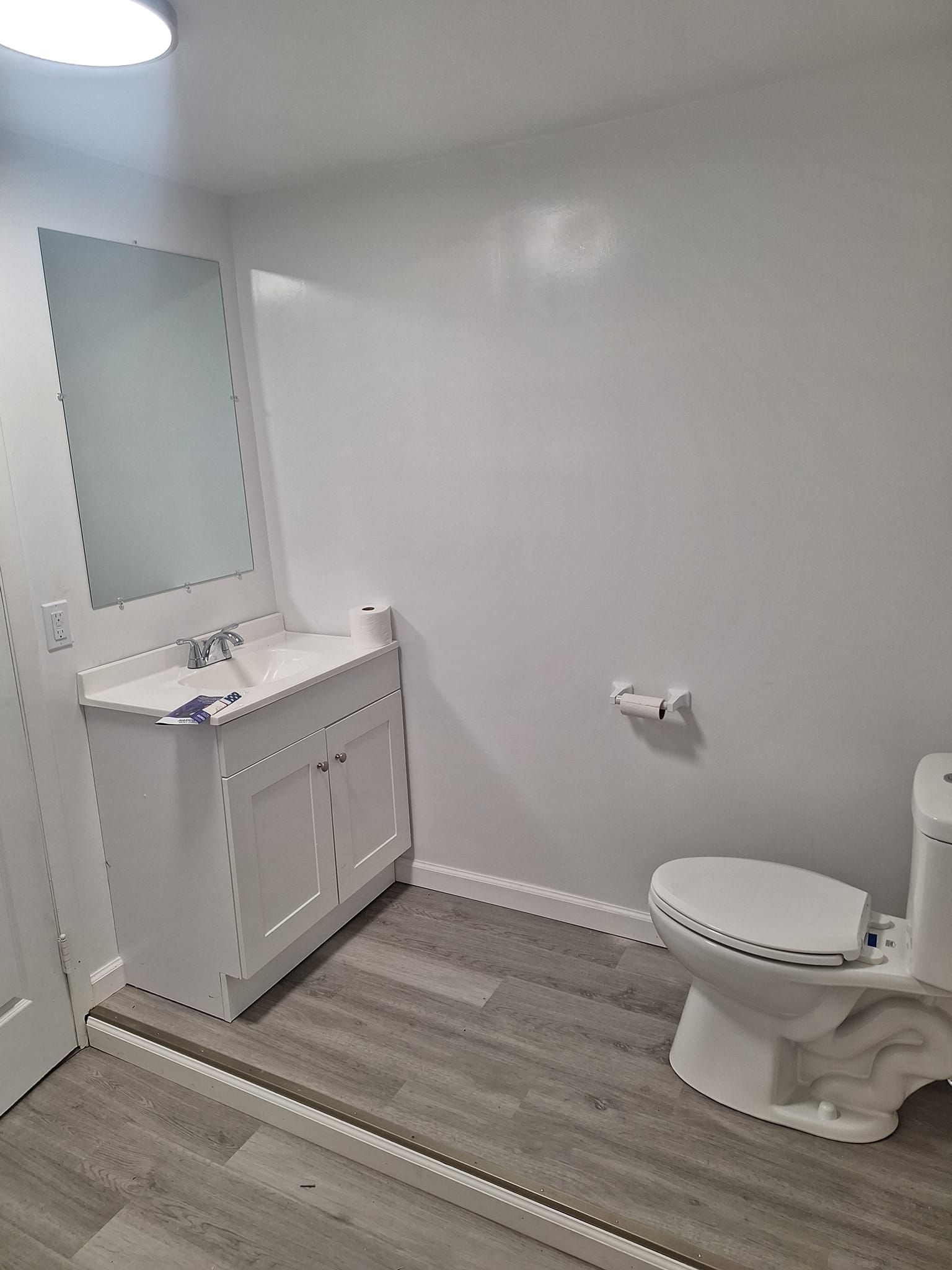 A modern bathroom featuring a white vanity with a mirror, a toilet, and gray wood-look flooring.