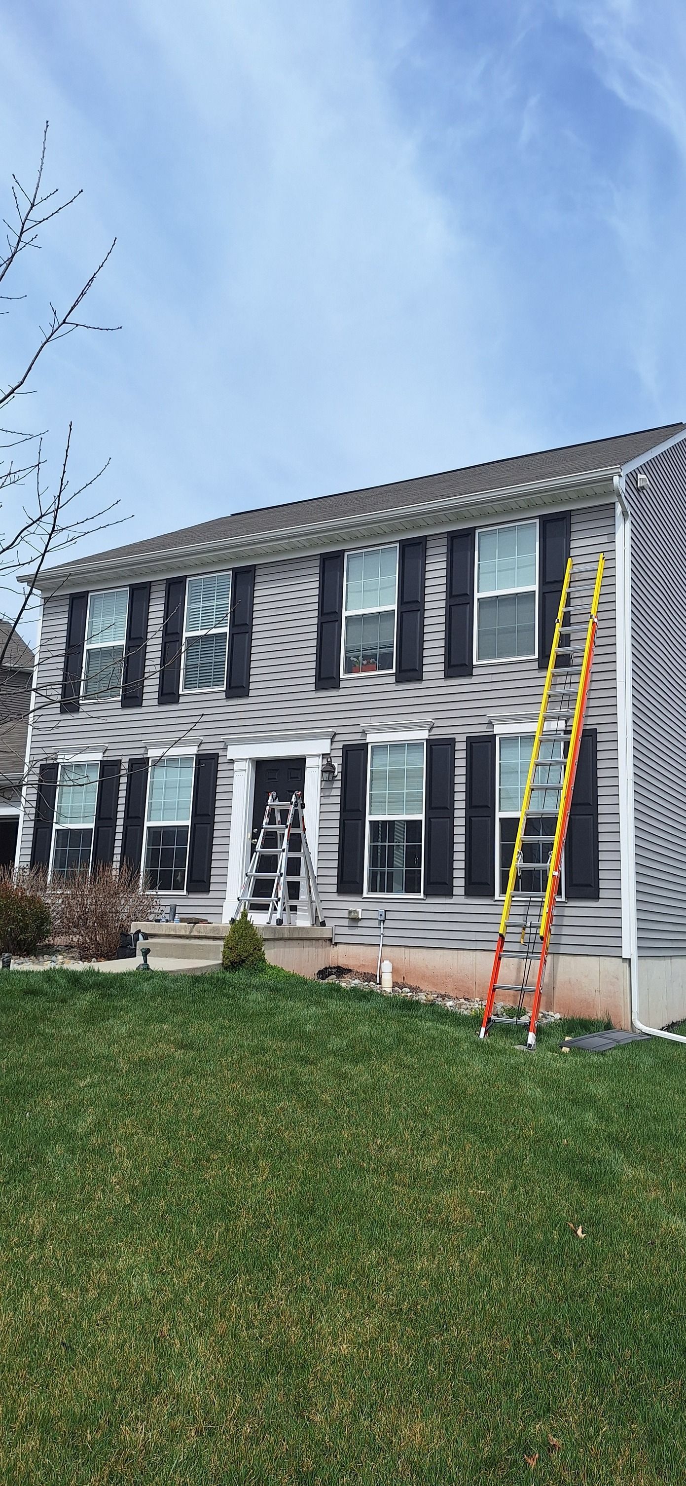 A two-story house undergoing exterior renovations with protective covering on the walls and an orange ladder leaning on it.