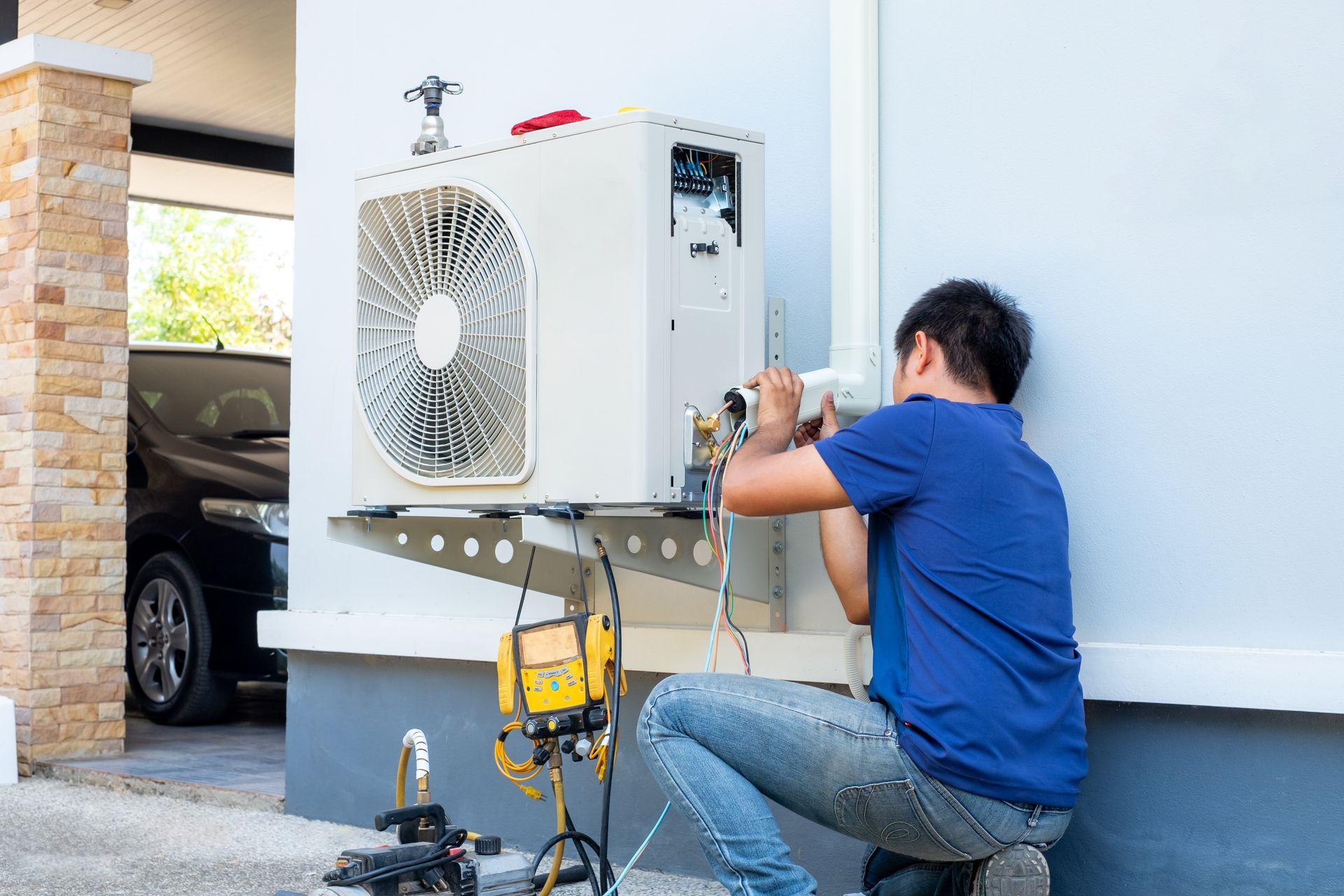 A technician repairing an air conditioning unit using electrical tools in a workshop.