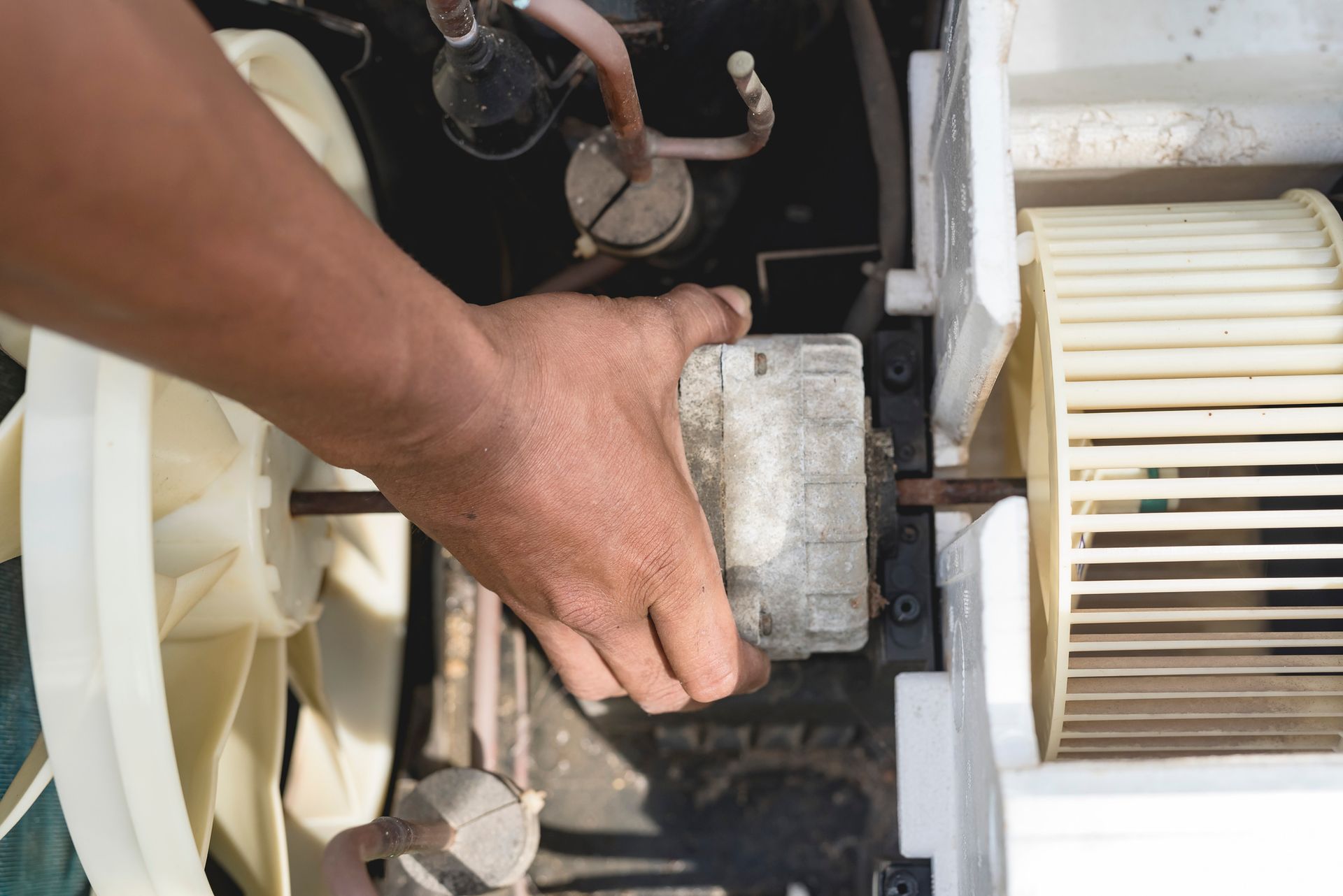 A repairman removes the motor, blower and condenser fan from a window type AC for repair services. A repairman removes the motor, blower and condenser fan from a window type AC for repair services.