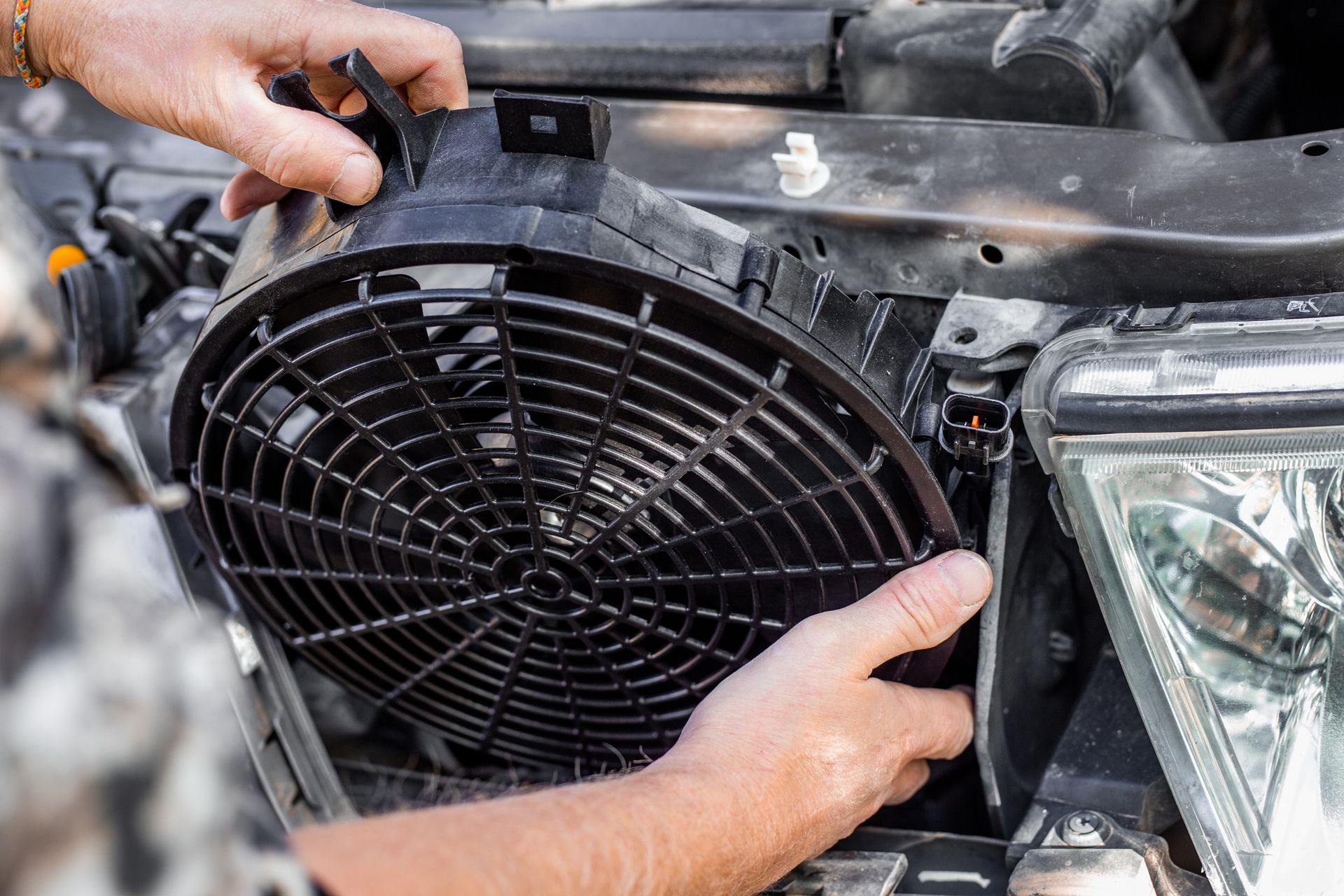 A man inserts an engine cooling fan under the radiator grill of a car.