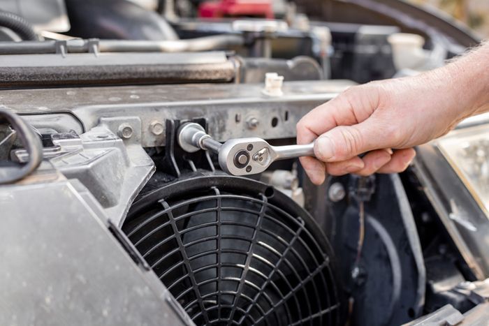 A man fixes an engine cooling fan under the radiator grill of a car. A man fixes an engine cooling fan under the radiator grill of a car.