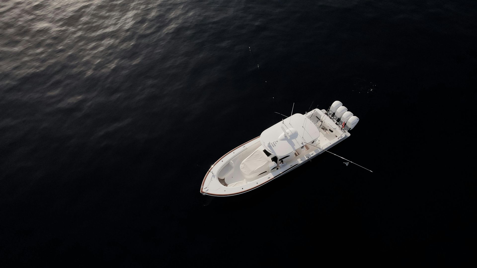 White boat with three engines on dark ocean water.