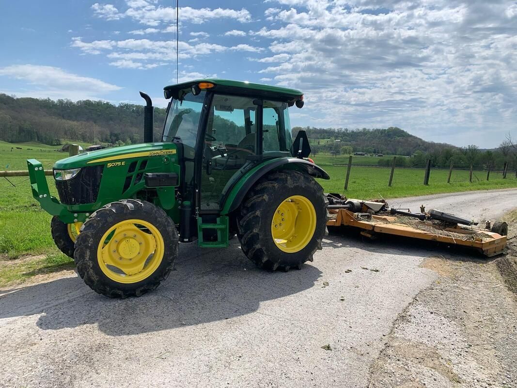 A green and yellow tractor is parked on the side of a road.