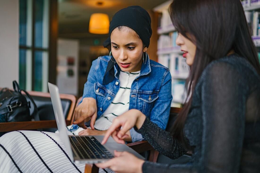 Two women are sitting at a table looking at a laptop computer.