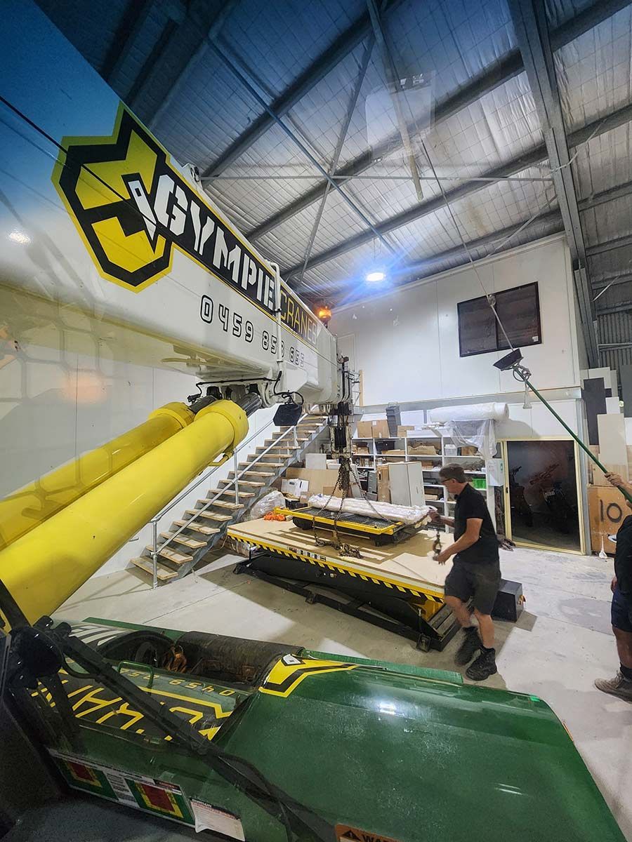 A Man Is Working On A Green And Yellow Vehicle In A Warehouse — Gympie Crane Hire In Glanmire, QLD