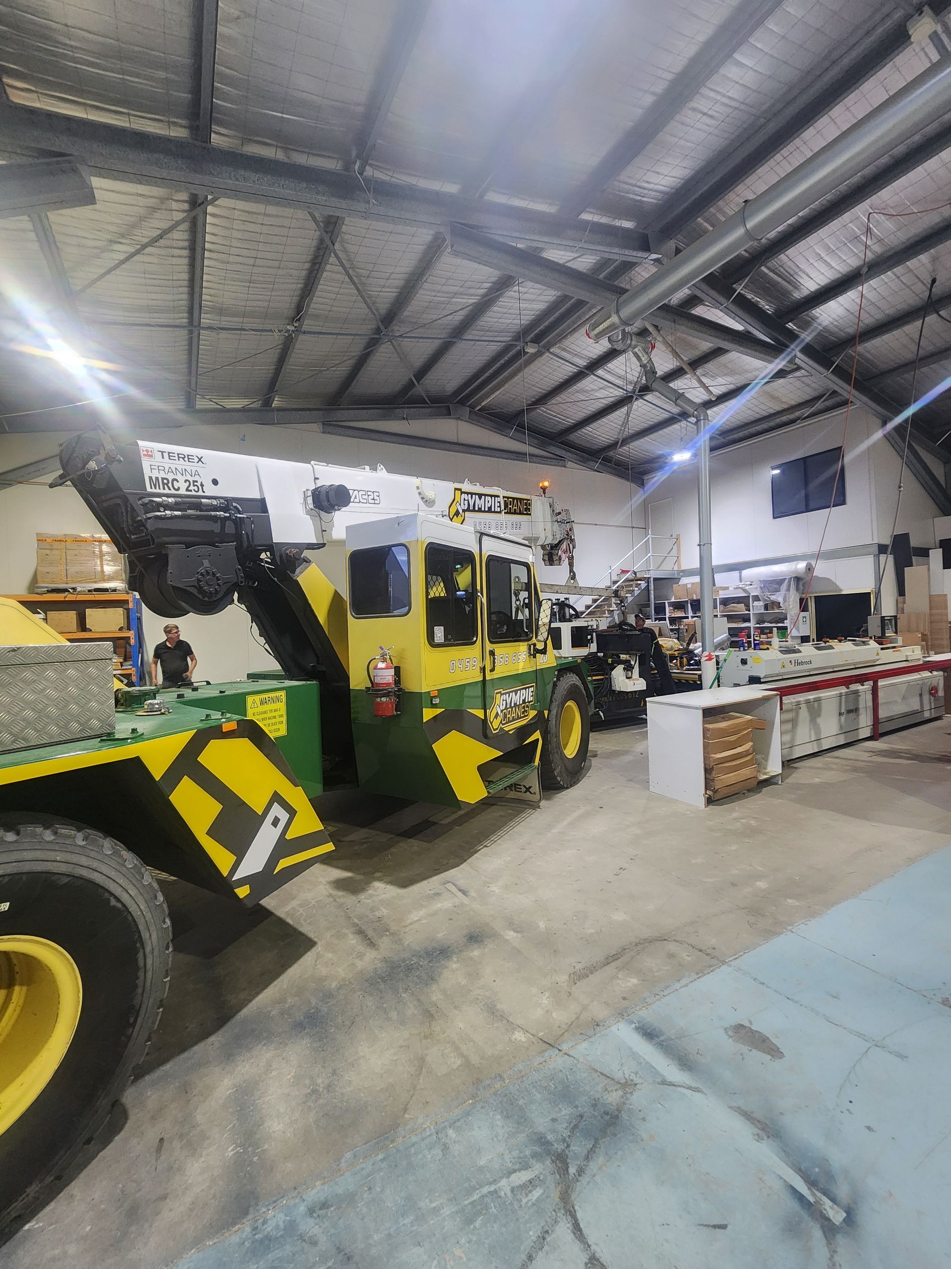 A Yellow Aerial Lift Is Parked In A Shed — Gympie Crane Hire In Glanmire, QLD
