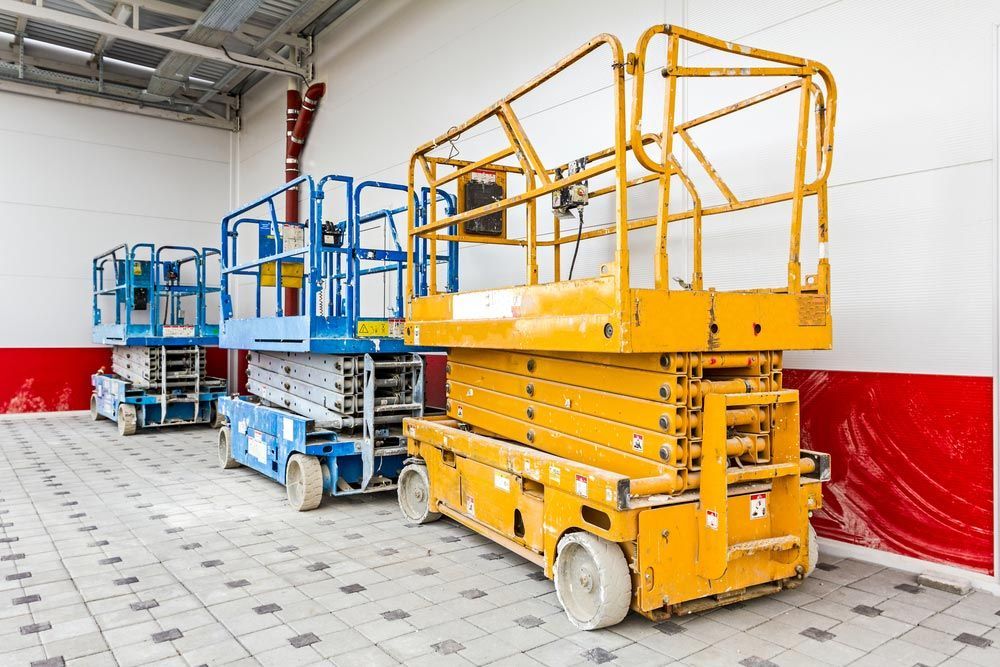 A Row Of Scissor Lifts Are Parked In A Warehouse — Gympie Crane Hire In Glanmire, QLD