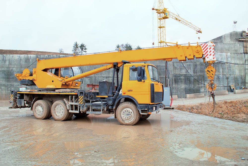 A Yellow Truck With A Crane Attached To It Is Parked On A Construction Site — Gympie Crane Hire In Glanmire, QLD