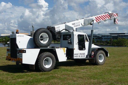 A White Truck With A Crane On The Back Is Parked In A Grassy Field — Gympie Crane Hire In Glanmire, QLD