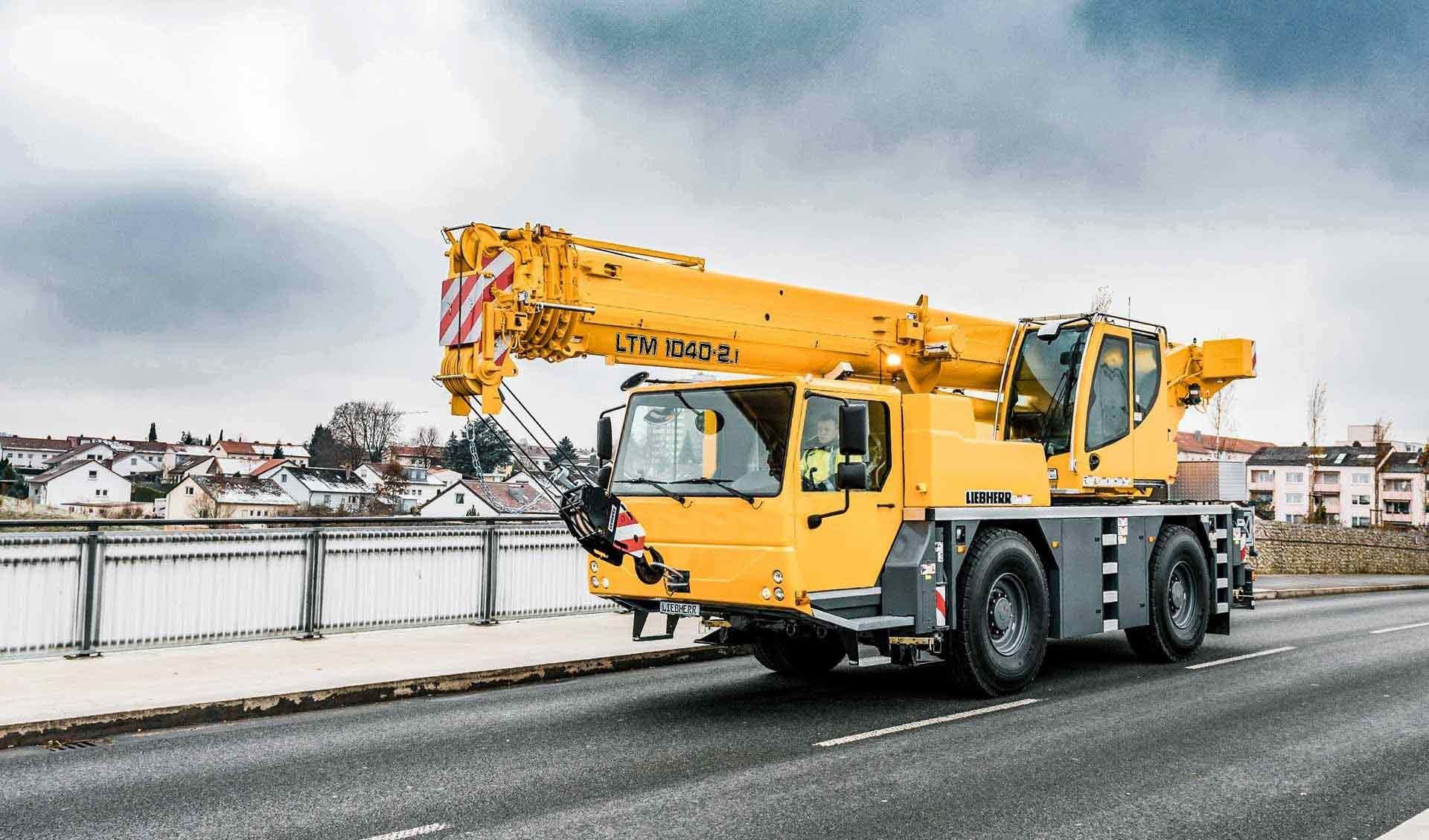 A Yellow Truck With A Crane On The Back Is Driving Down A Road — Gympie Crane Hire In Glanmire, QLD