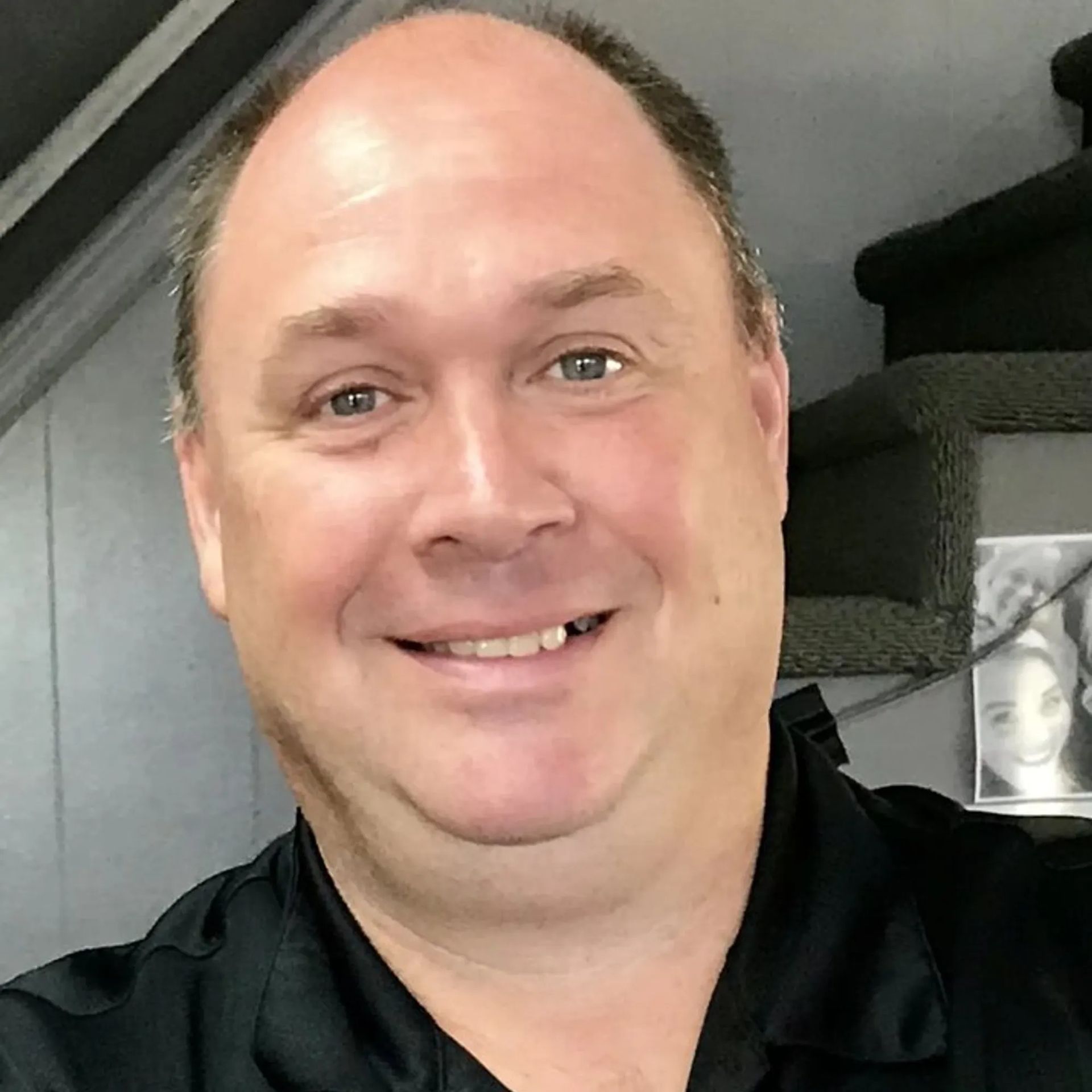 A bald man in a black shirt is smiling for the camera.