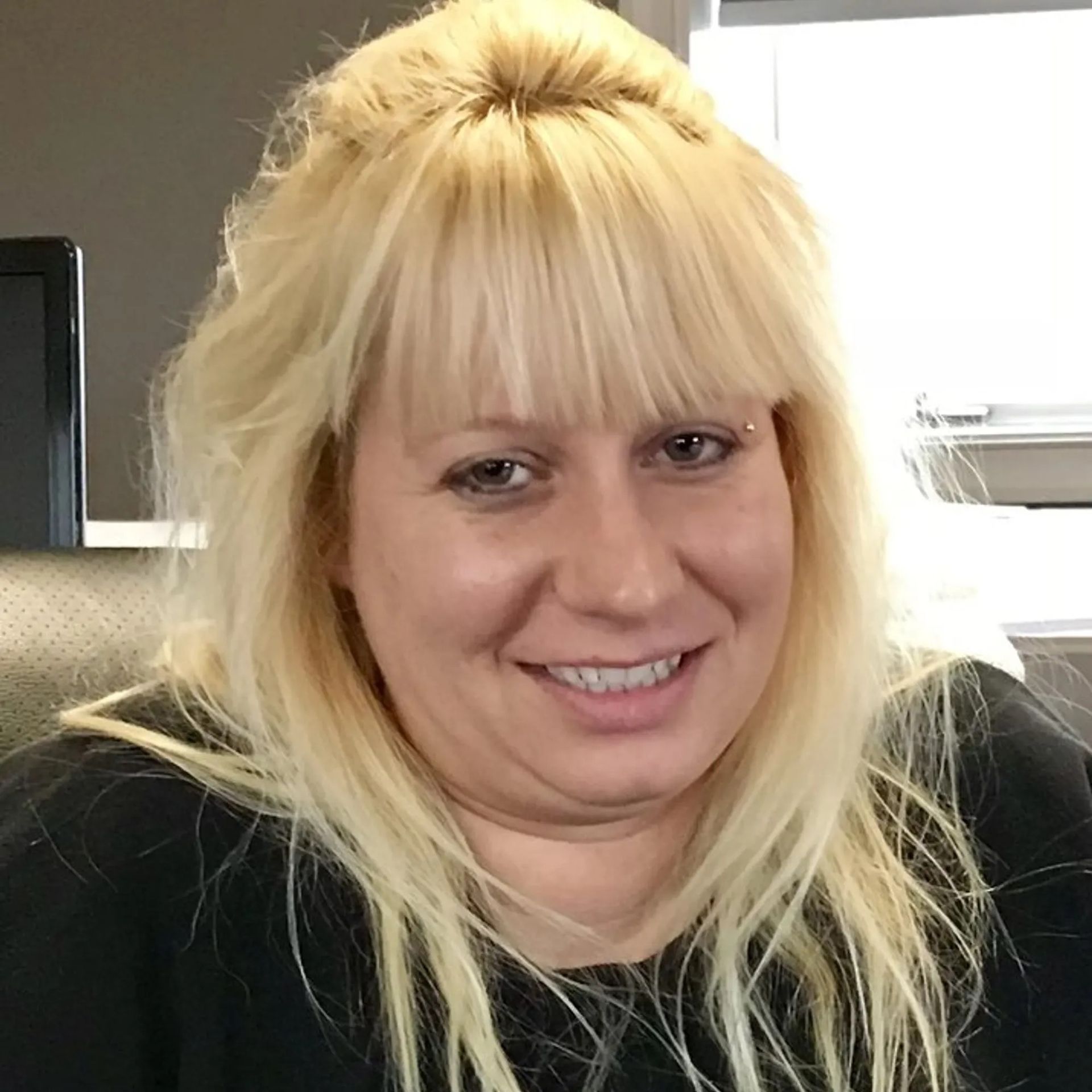 A woman with blonde hair and bangs is smiling for the camera
