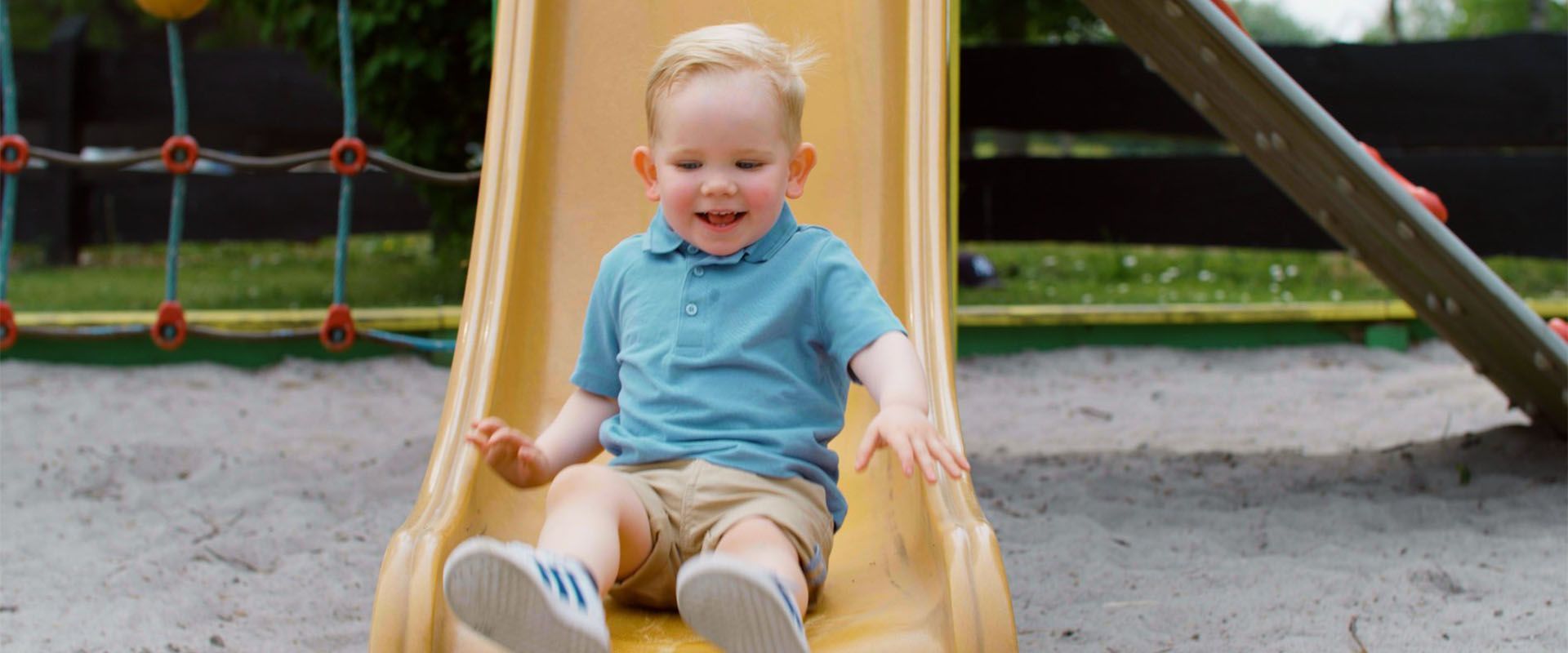 A young boy is sitting on a yellow slide at a playground.