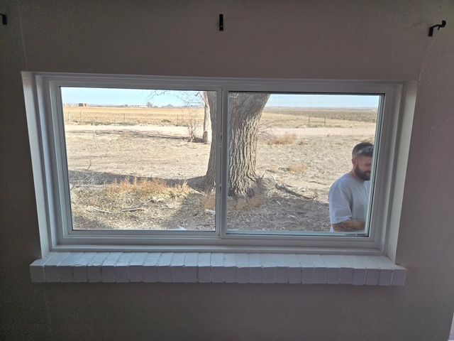 Window view of a rural yard with a tree and a person standing outside on the right