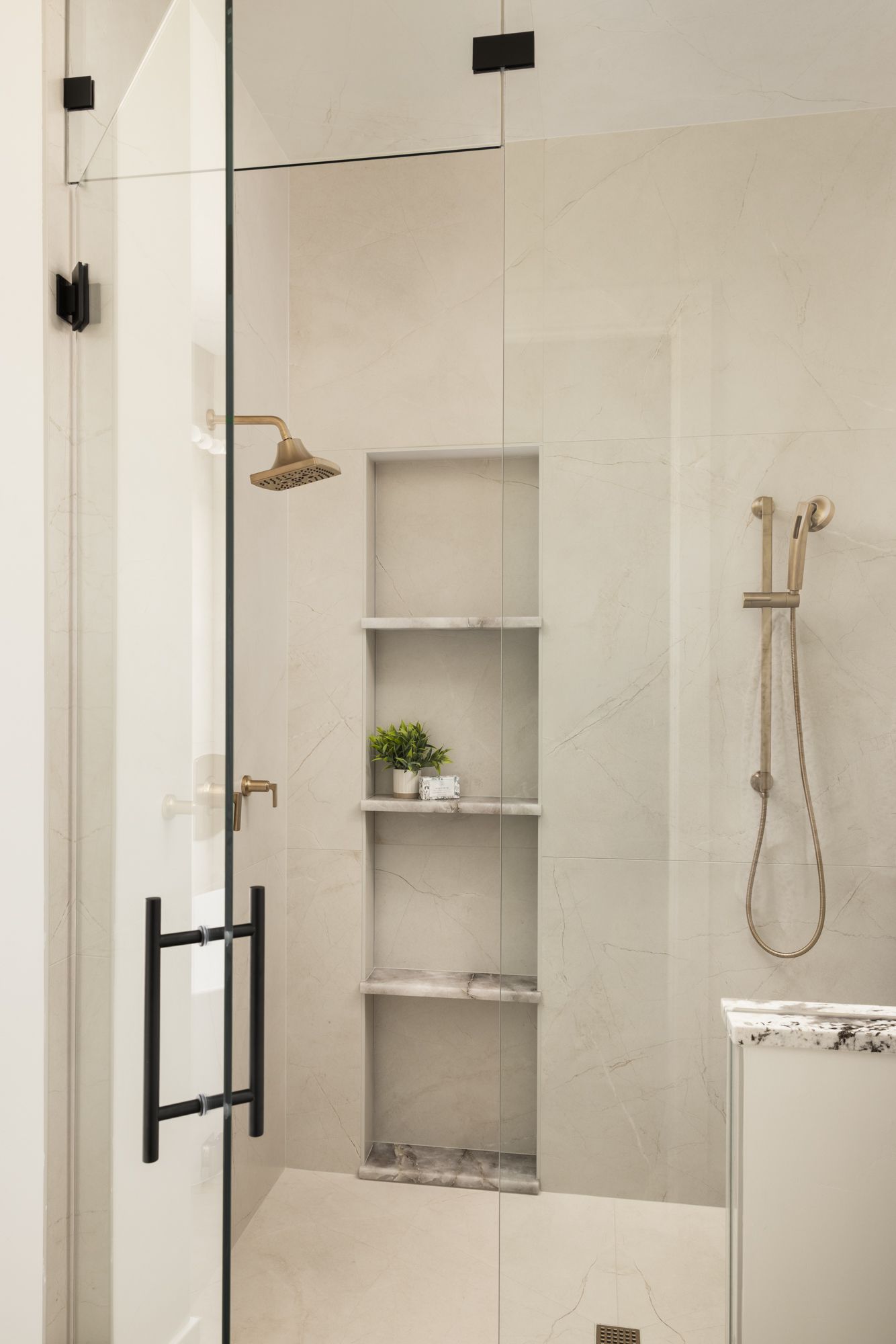 Modern bathroom shower with beige tile, built-in niches, and black glass door handles