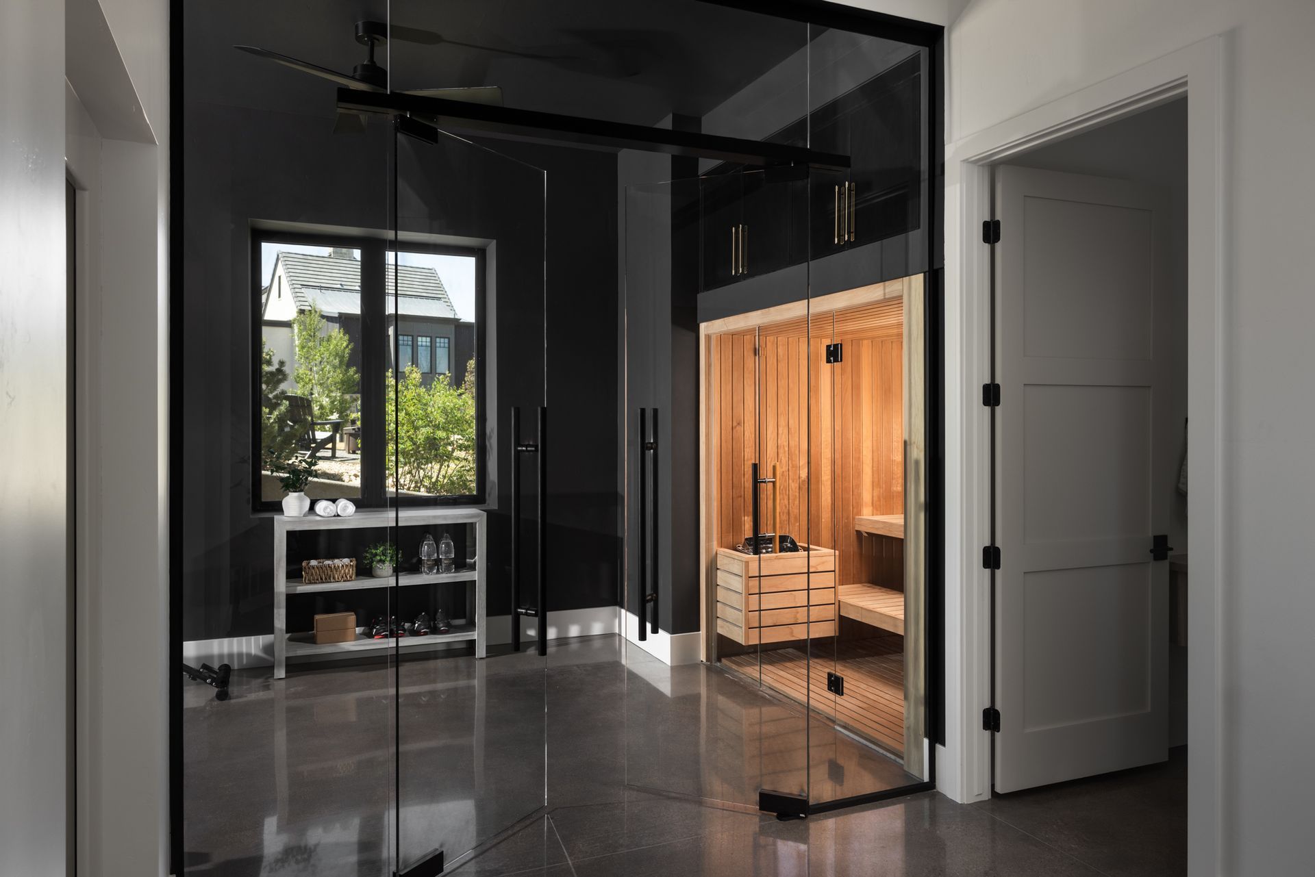 Modern home interior with dark walls, glossy floor, and a lit wood-paneled room behind glass doors
