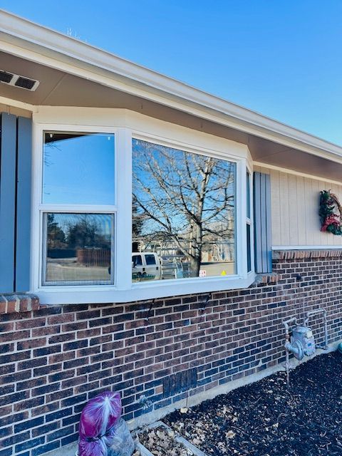 Brick house exterior with a bay window reflecting trees and a clear blue sky